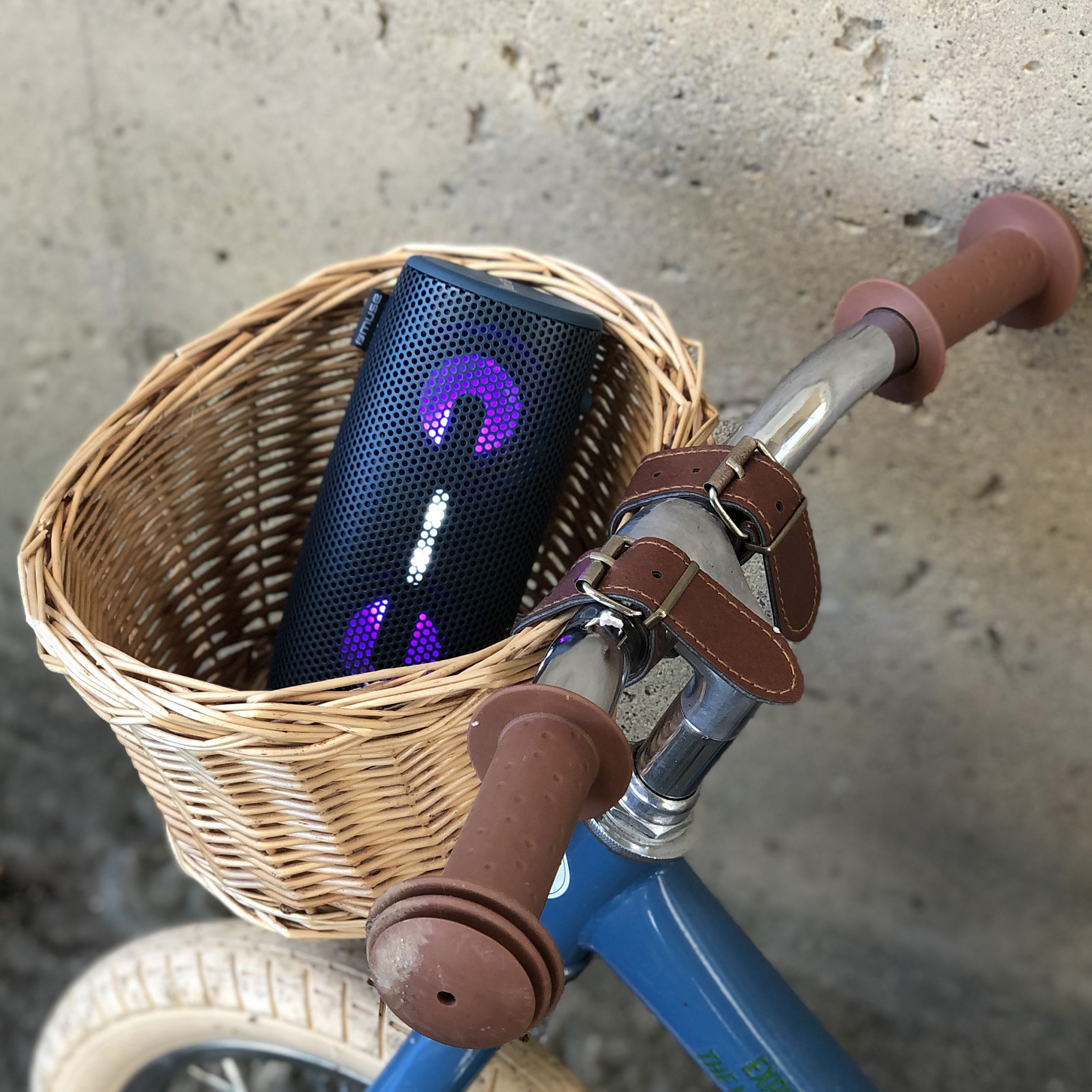 Głośnik w wiklinowym koszu na niebieskim rowerze. Głośnik jest czarny z fioletowymi światłami.