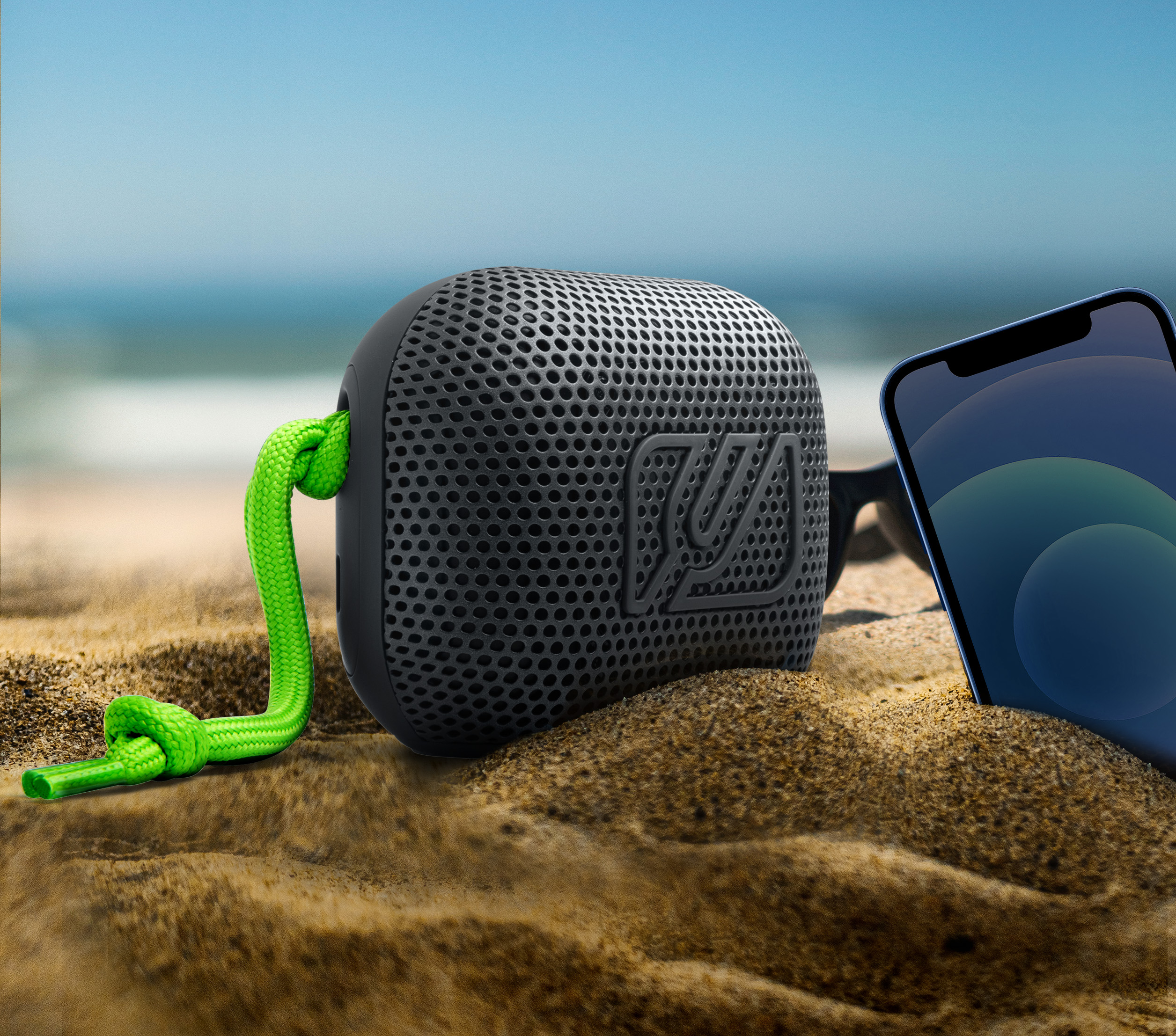 Czarny głośnik z zielonym przewodem, smartfon i tło plaży.