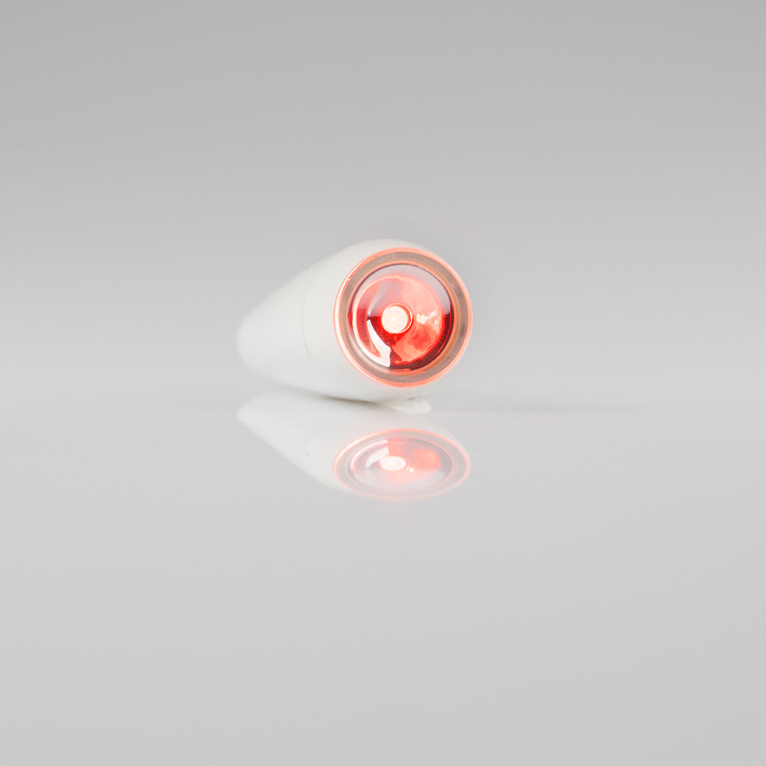 White, teardrop-shaped device with a red light on a white reflective surface.