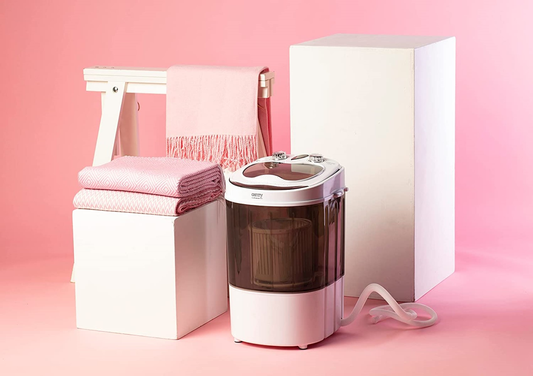Rosa Artikel: Decken, ein weißer Hocker und eine Waschmaschine vor rosa Hintergrund.