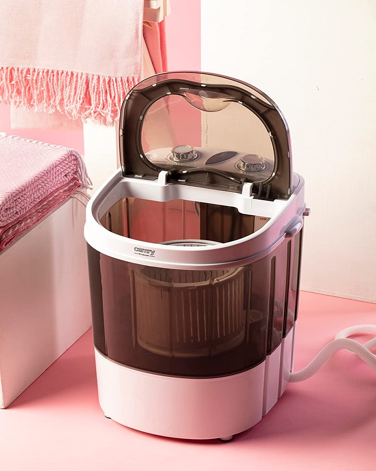 Eine kleine Waschmaschine mit offenem Deckel auf rosa Oberfläche.