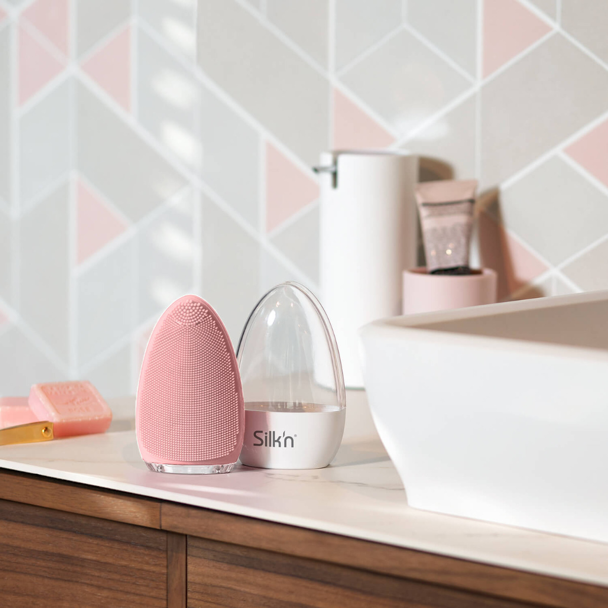 Eine rosa Gesichtsreinigungsbürste neben einem transparenten Behälter mit Wasser und Seife.