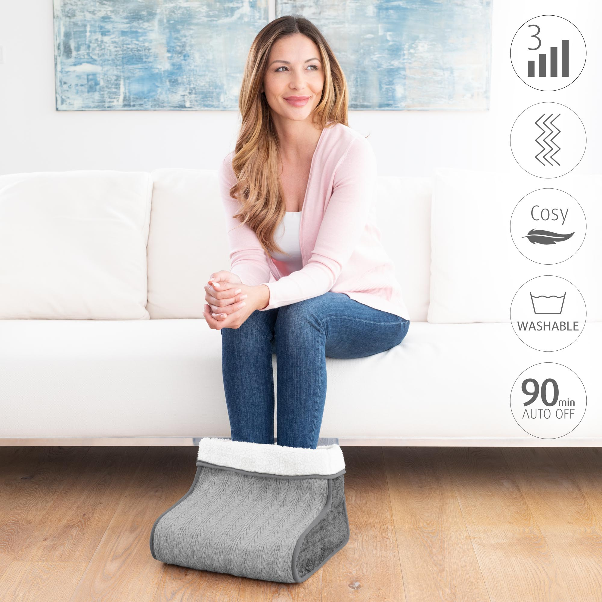 Mujer sentada en el sofá con calentador de pies. Iconos: 3 barras, zigzag, pluma, gota de agua y 90 min apagado automático.