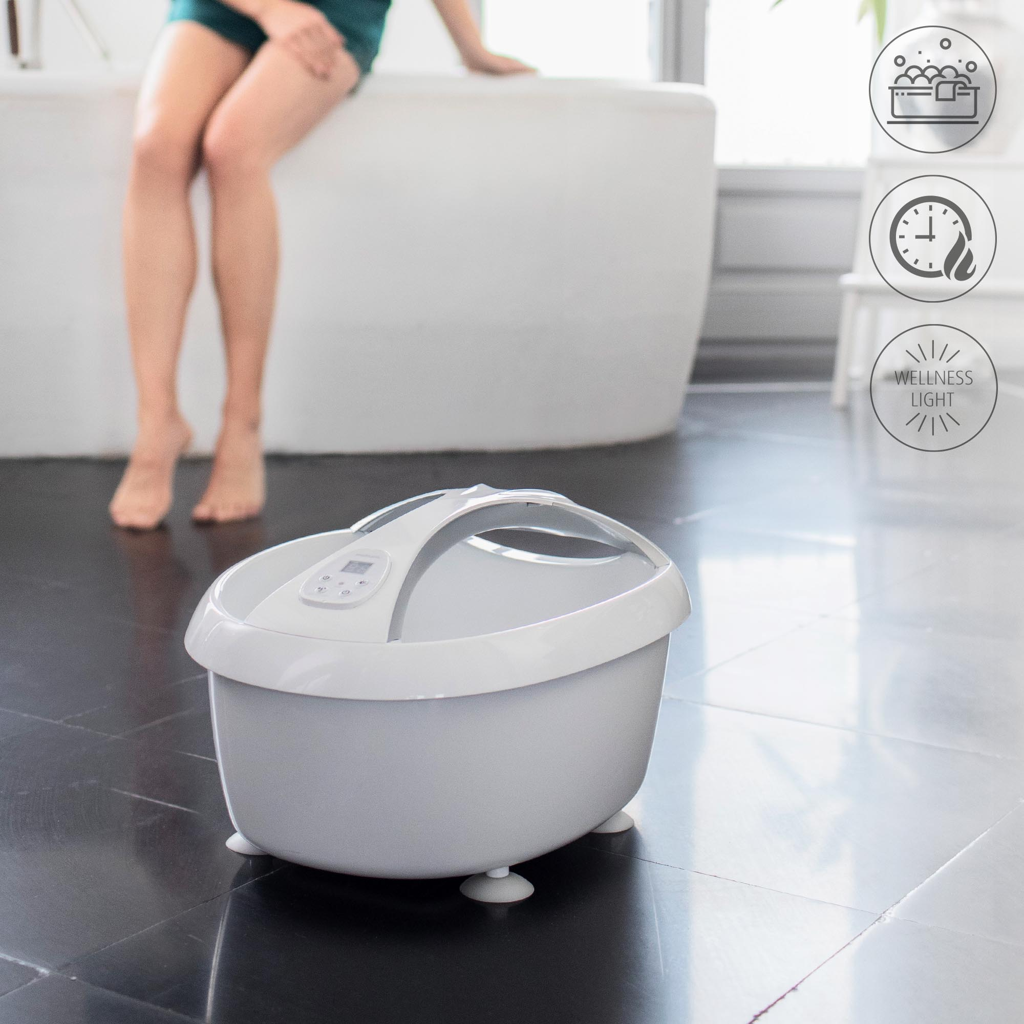 A foot spa and a woman sitting on the edge of a bathtub. There are some bubbles on the right.