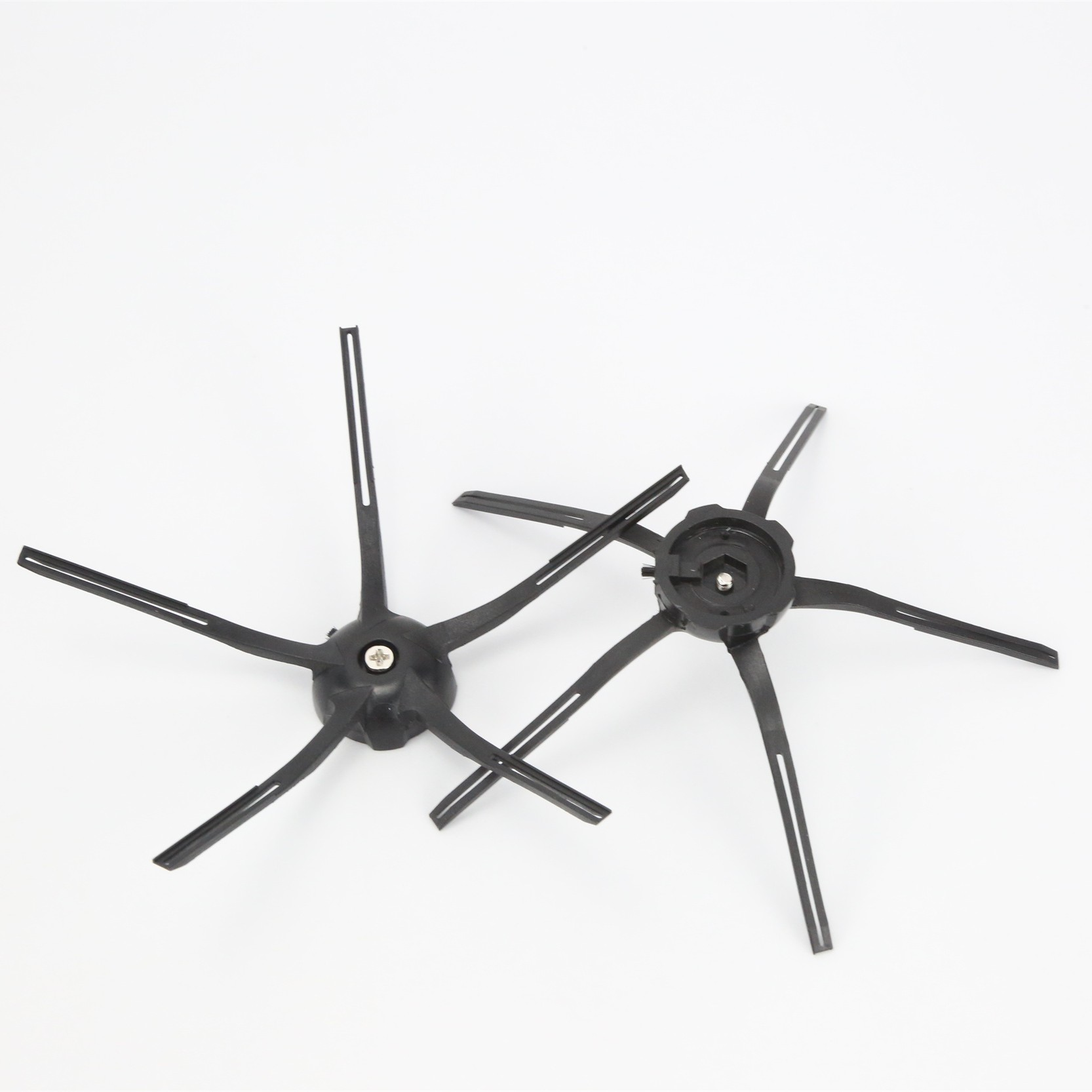 Dwie czarne szczotki do robota sprzątającego. W kształcie gwiazdy z wieloma ramionami. Na białym tle.