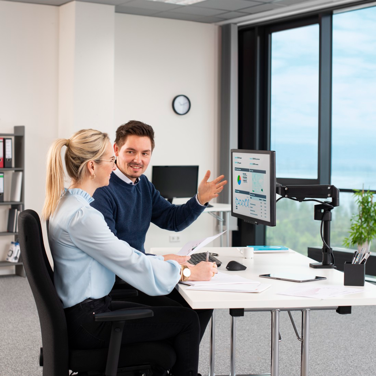 Dwie osoby w biurze, patrzące na ekran komputera. Jedna wskazuje, druga pisze.