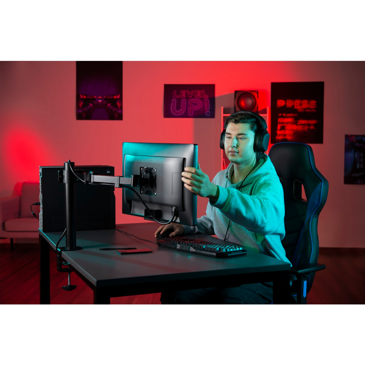 Gracz przy biurku regulujący monitor. Pokój oświetlony na czerwono z widoczną klawiaturą, krzesłem i komputerem.