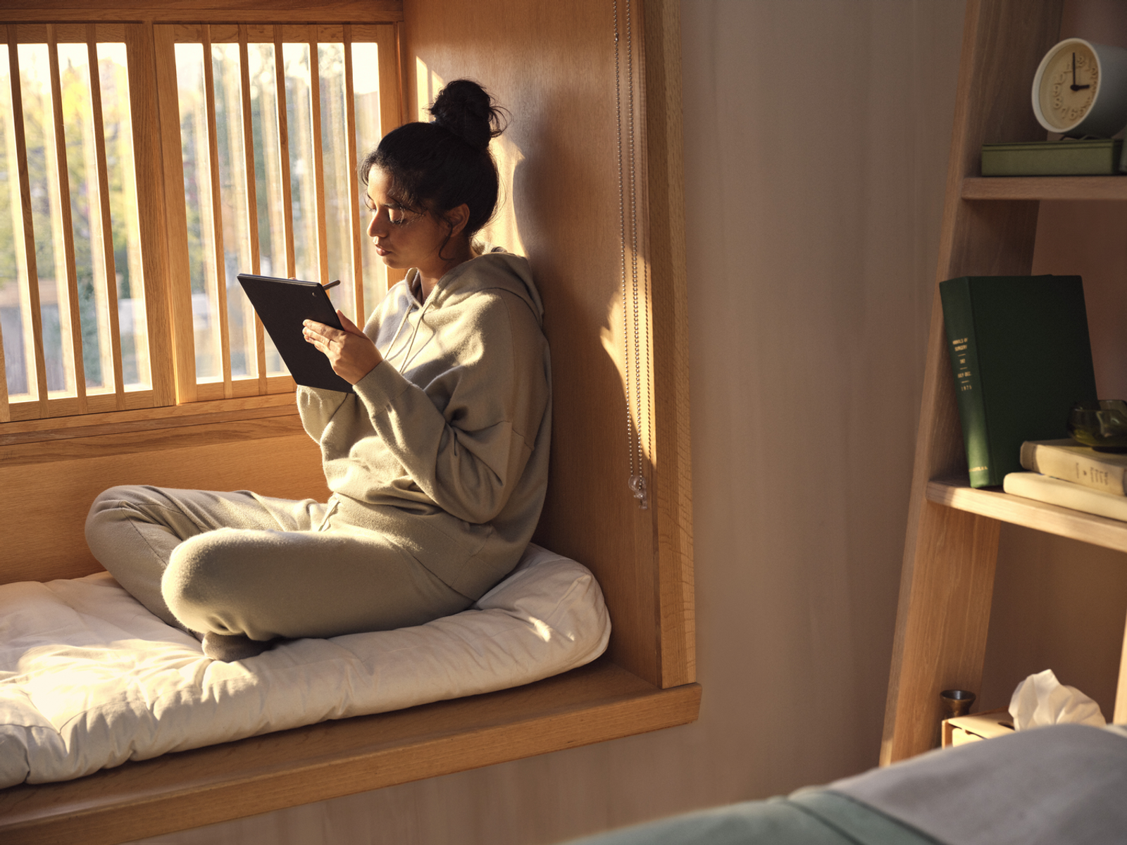Kobieta siedząca przy oknie czyta tablet. Wchodzi światło słoneczne.