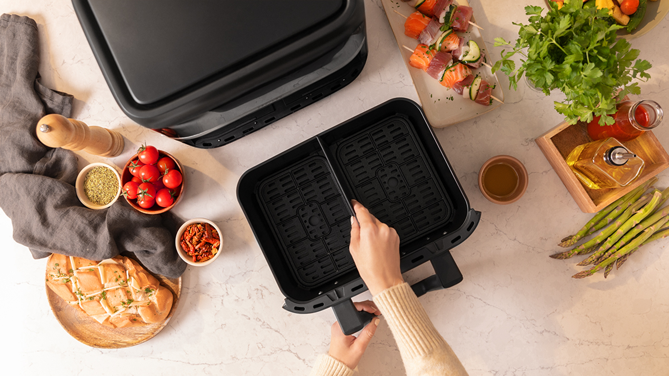 Vista superior de una freidora de aire con alimentos e ingredientes. Manos de una persona cerca de la cesta.