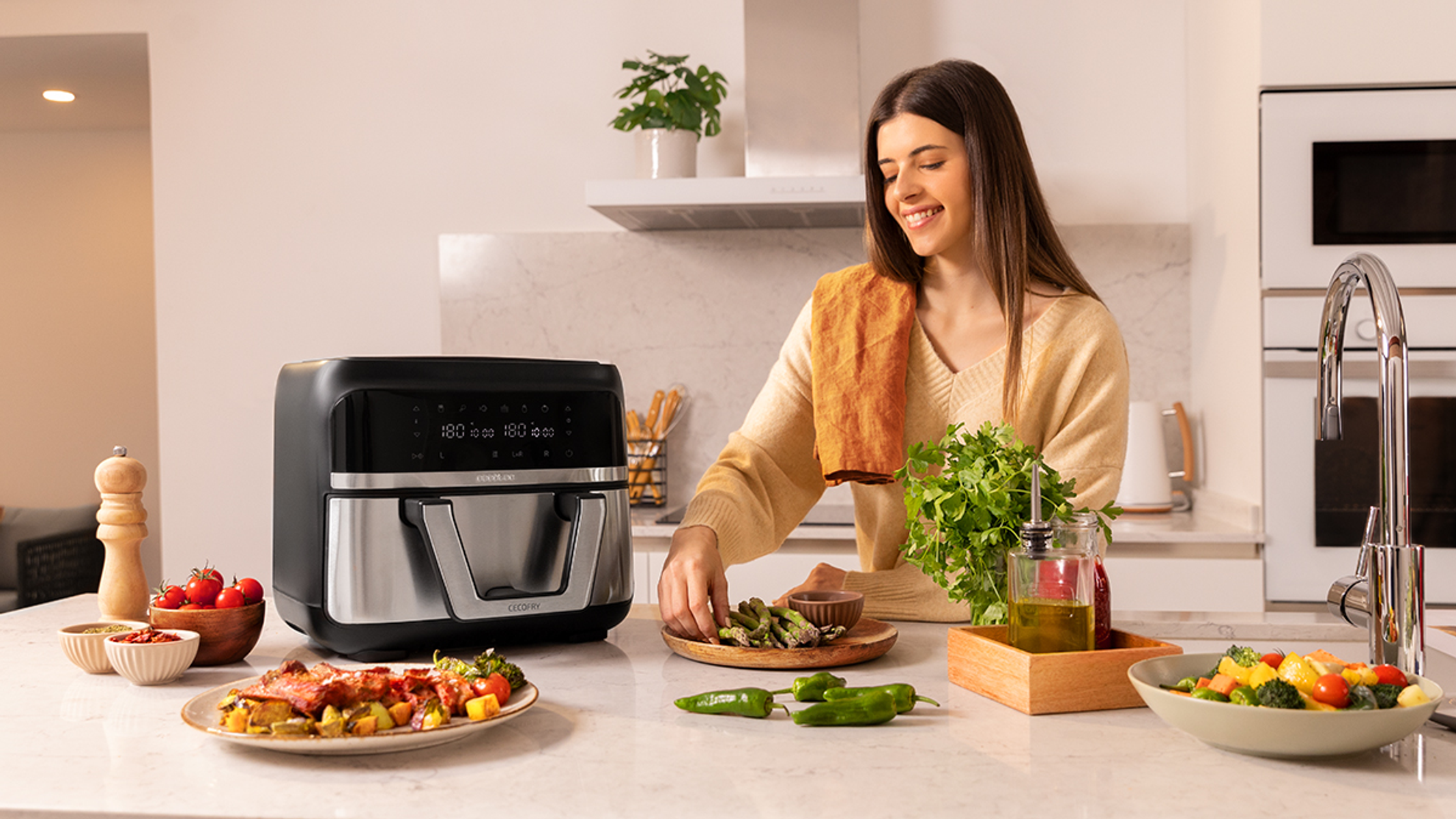 Mujer en cocina con encimera, freidora y platos de comida.