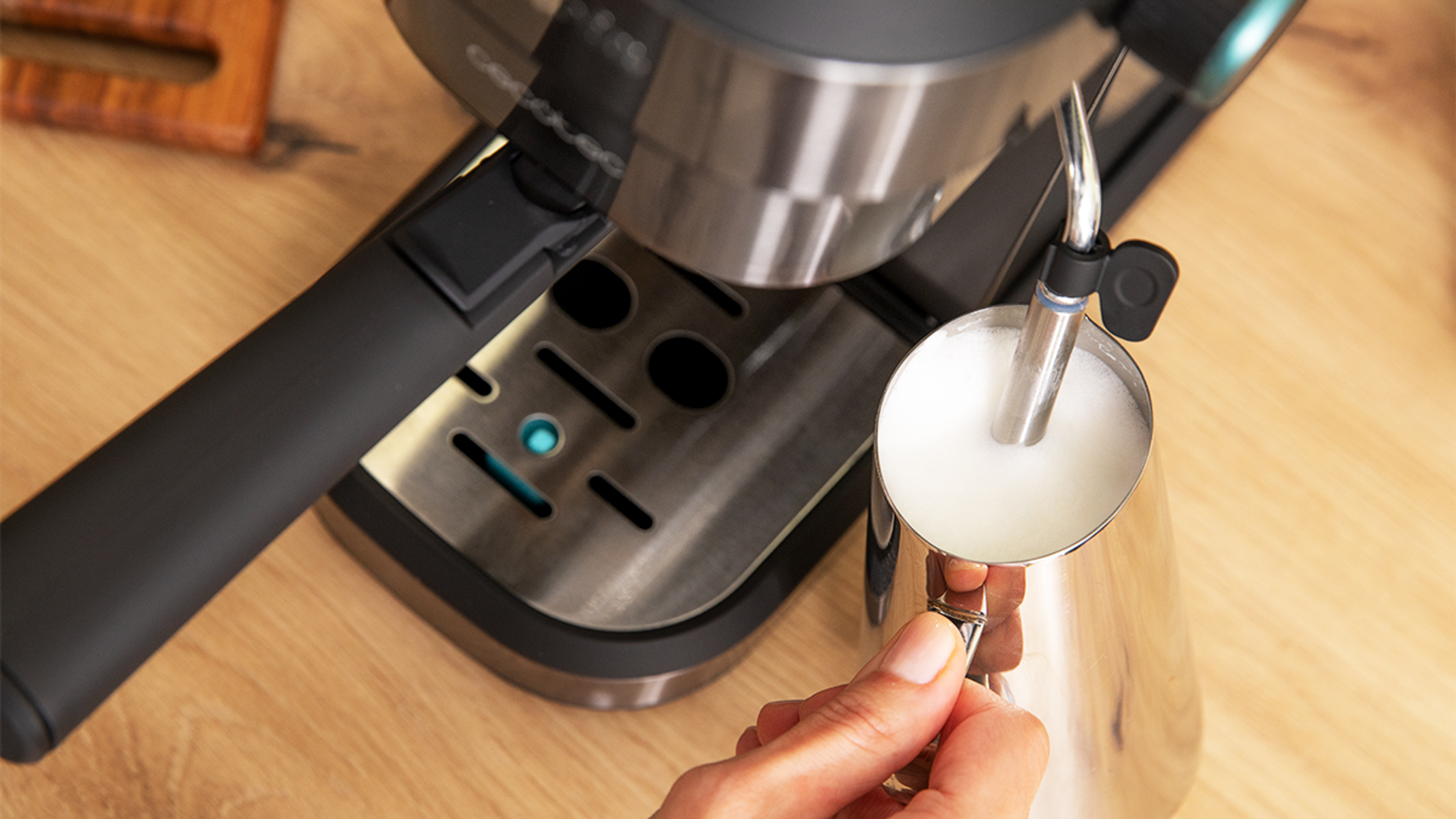 Ekspres do kawy z ręką spieniającą mleko w metalowym dzbanku, na drewnianym stole.