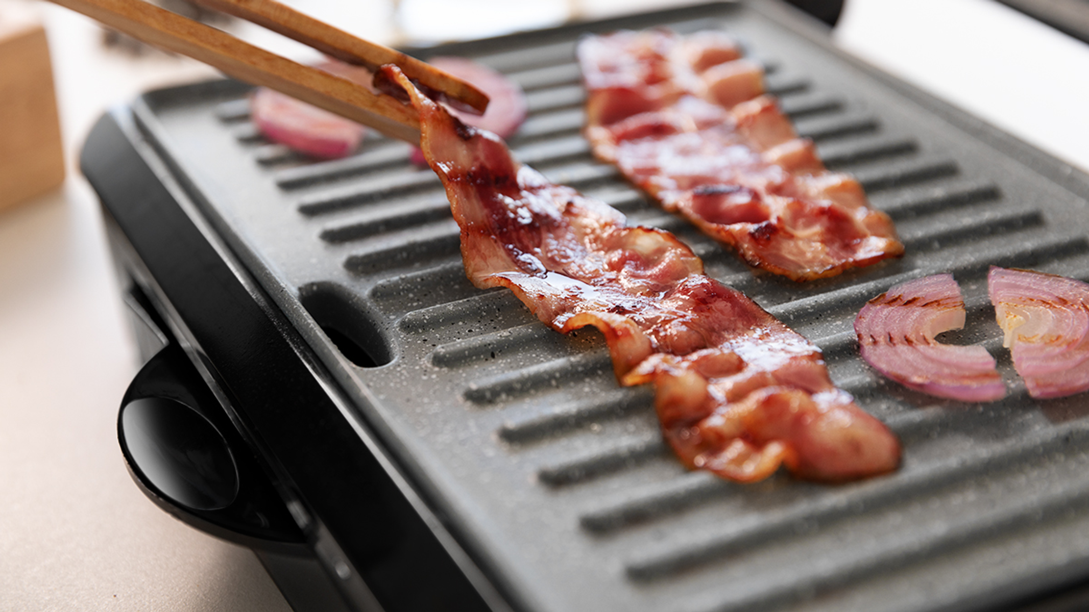 Grill z boczkiem i czerwoną cebulą. Pałeczki trzymają plasterek boczku.