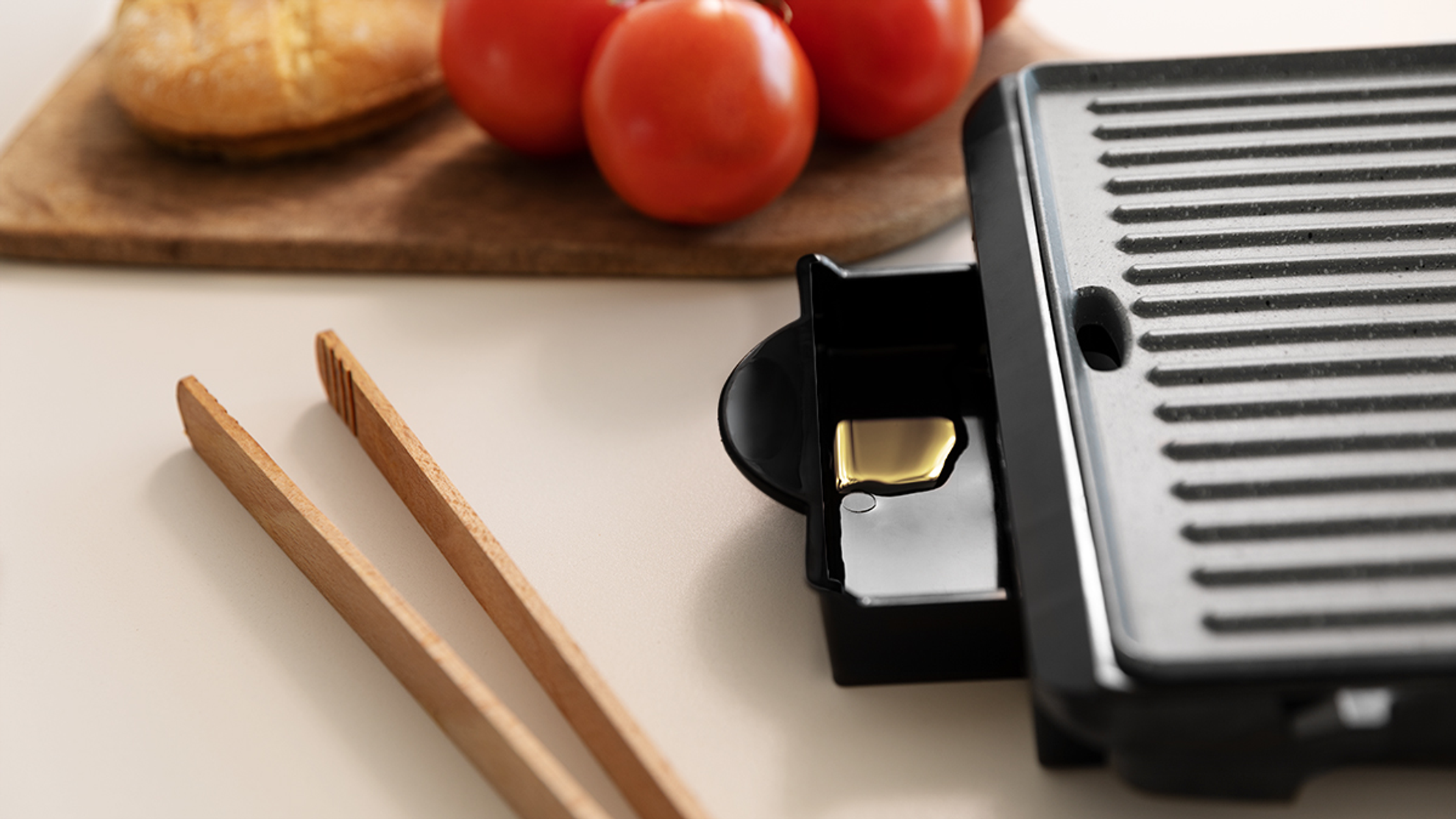 Zbliżenie na grill z pomidorami, chlebem i szczypcami na białej powierzchni. Czarny grill i drewniane szczypce.