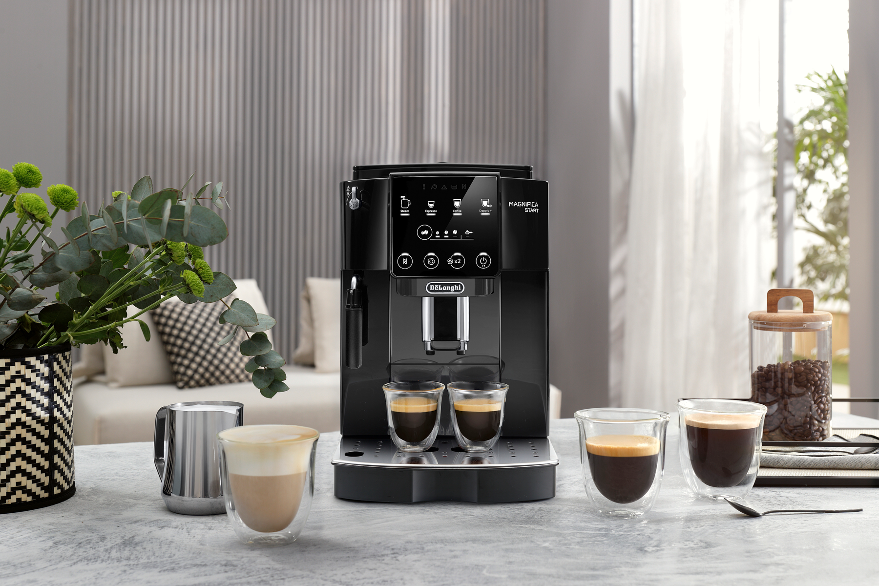 Eine schwarze Kaffeemaschine mit zwei Espressotassen. Links eine Blumenvase.