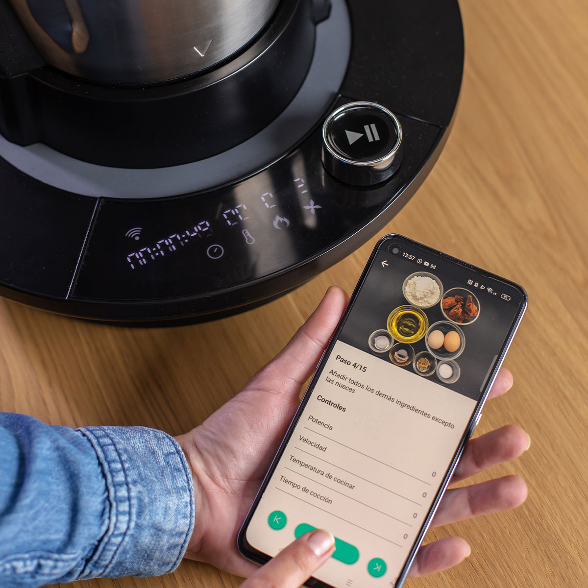 Osoba używająca smartfona do sterowania czarnym urządzeniem kuchennym z cyfrowym ekranem.
