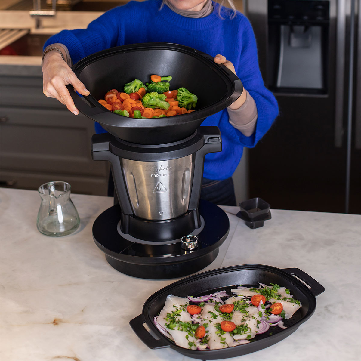 Osoba dodająca warzywa do urządzenia kuchennego z jedzeniem i tacą.