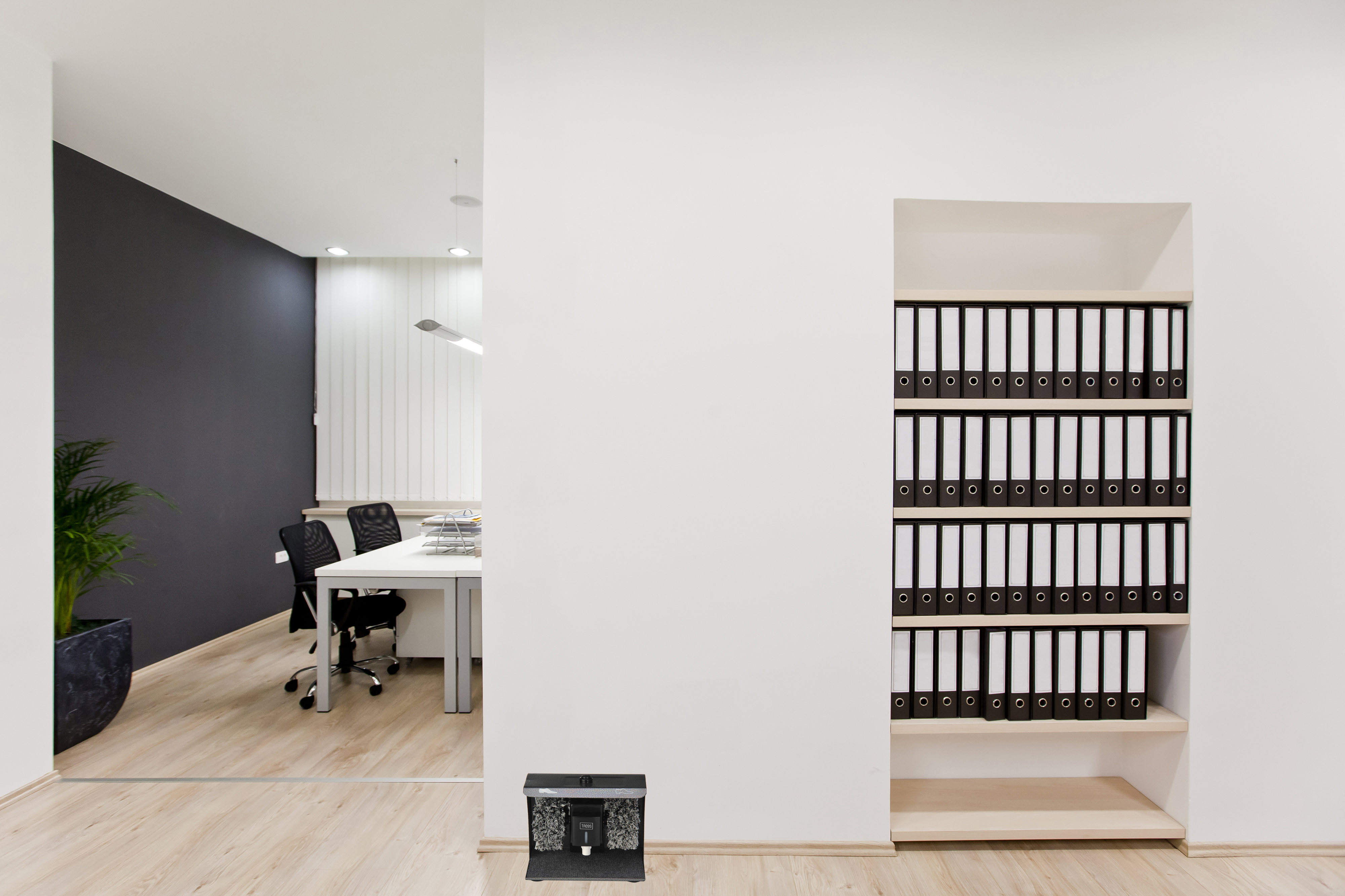 Ein Bürointerieur mit einem Flur, der zu einem Arbeitsbereich mit Schreibtisch und Stühlen führt.