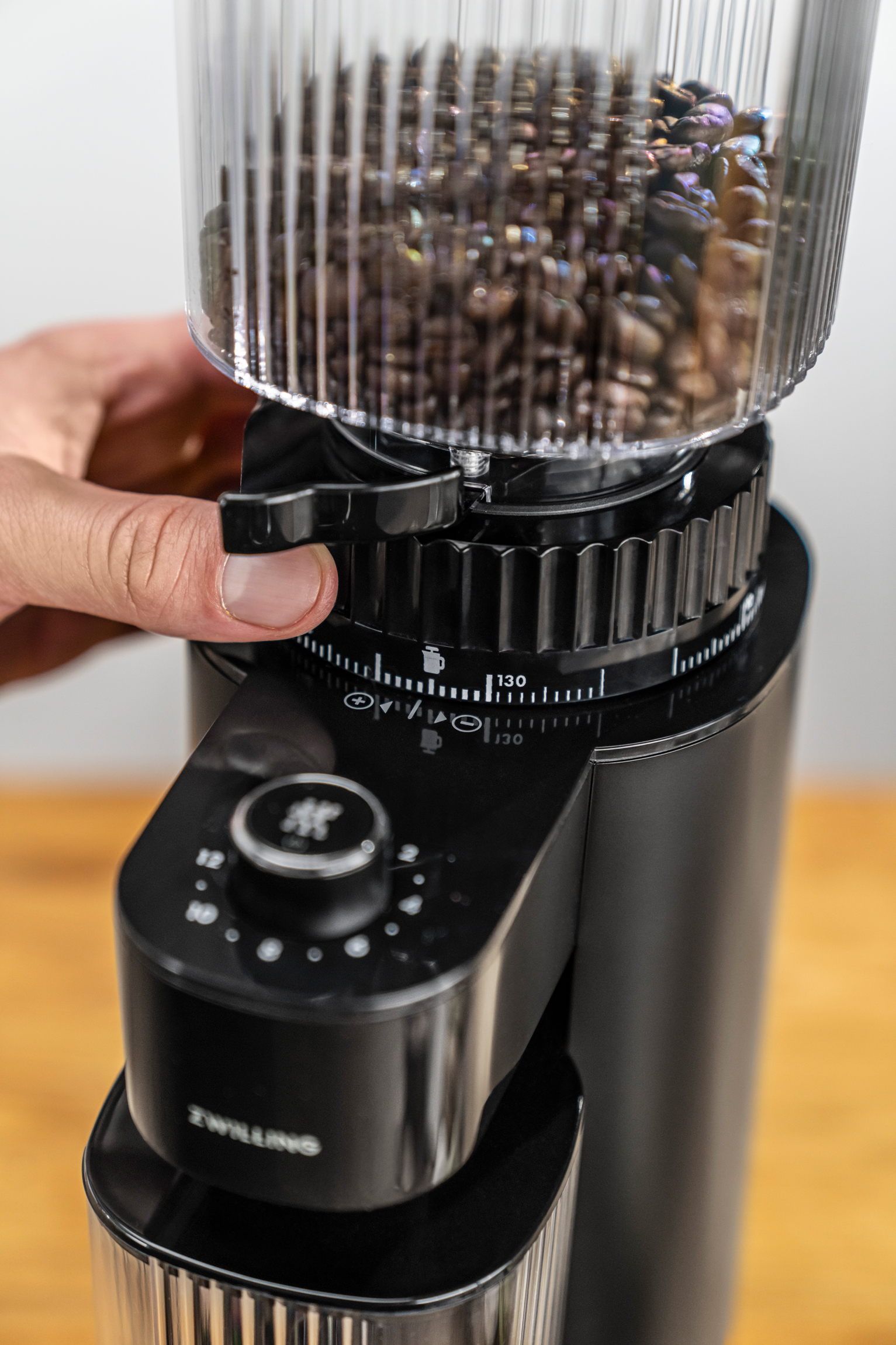 Mano de persona ajustando un molinillo de café negro, primer plano. Molinillo tiene diales.
