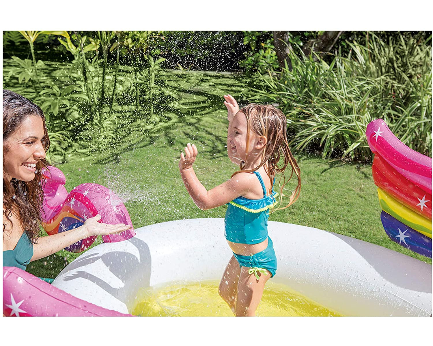 Eine Frau und ein Mädchen spielen in einem Einhorn-Pool. Das Mädchen spritzt Wasser.