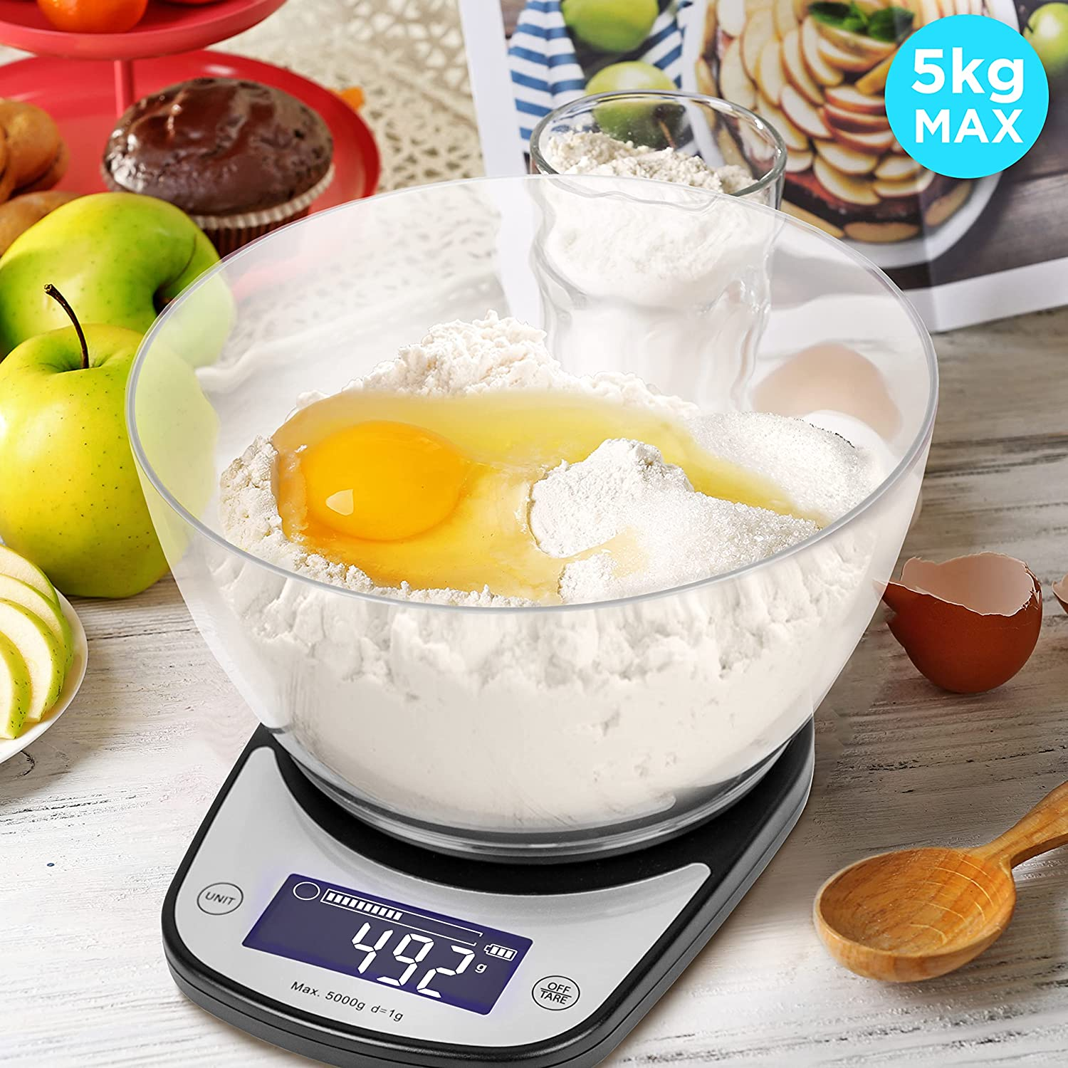 Digitale Küchenwaage mit Mehl, Ei und klarer Schüssel. Hintergrund Äpfel, Kuchen und ein Glas.
