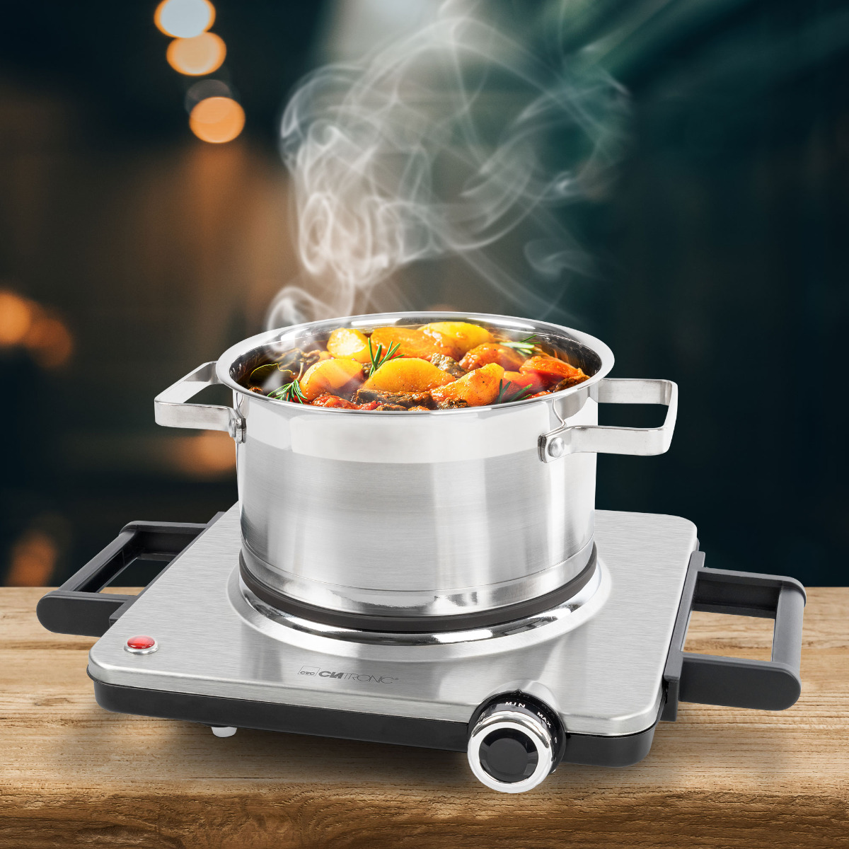 Srebrny garnek z jedzeniem na przenośnej kuchence. Para unosi się, na drewnianym stole.