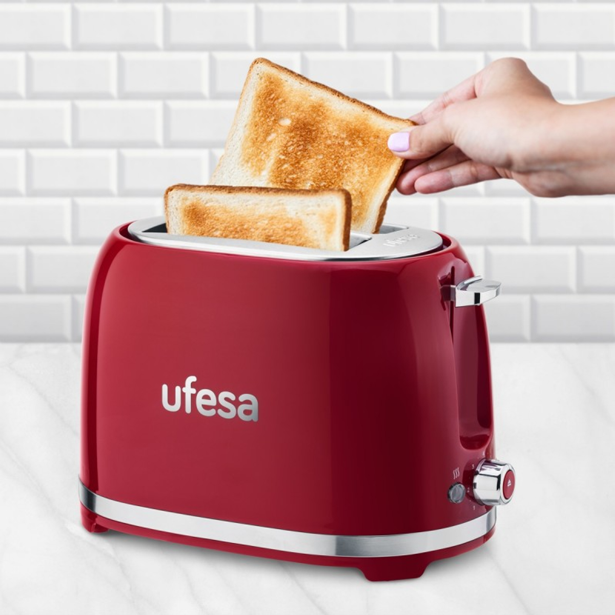 Czerwony toster Ufesa z tostami i ręką wyjmującą kromkę. W tle biała ceglana ściana.