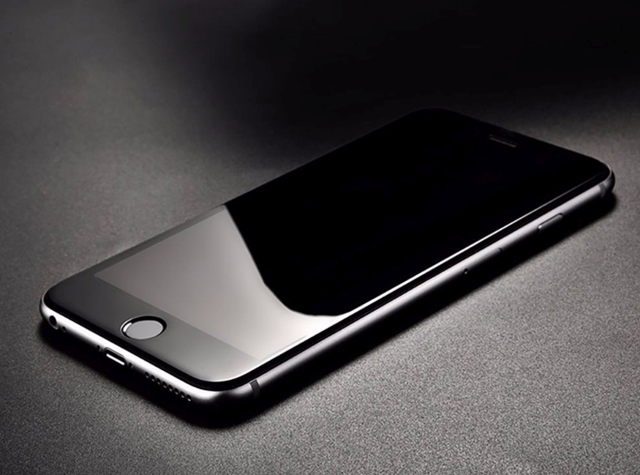 Schwarzes Smartphone auf dunkler Oberfläche, reflektiert Umgebungslicht.