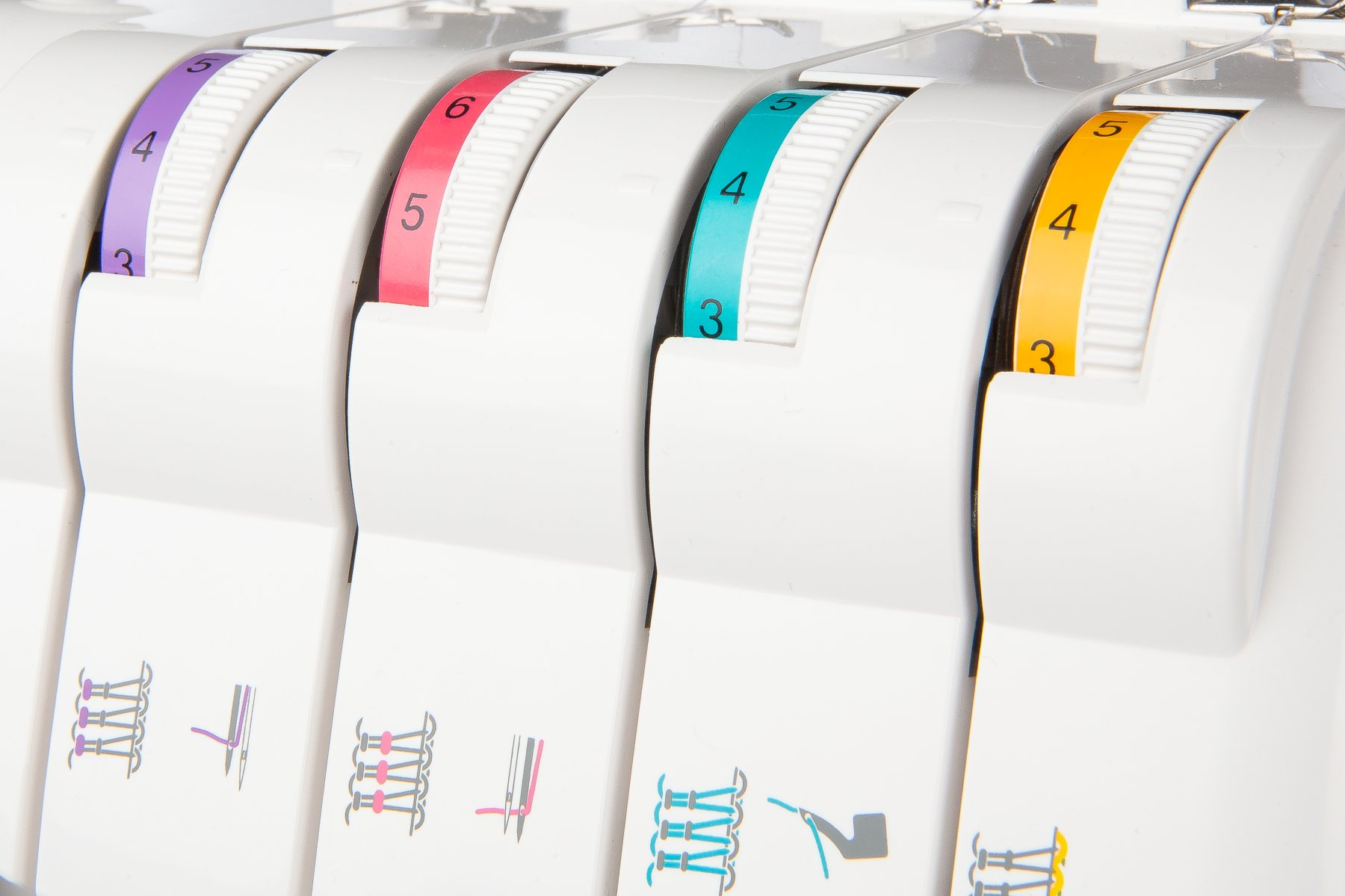 Zbliżenie pokręteł maszyny do szycia. Białe pokrętła z kolorowymi numerami.