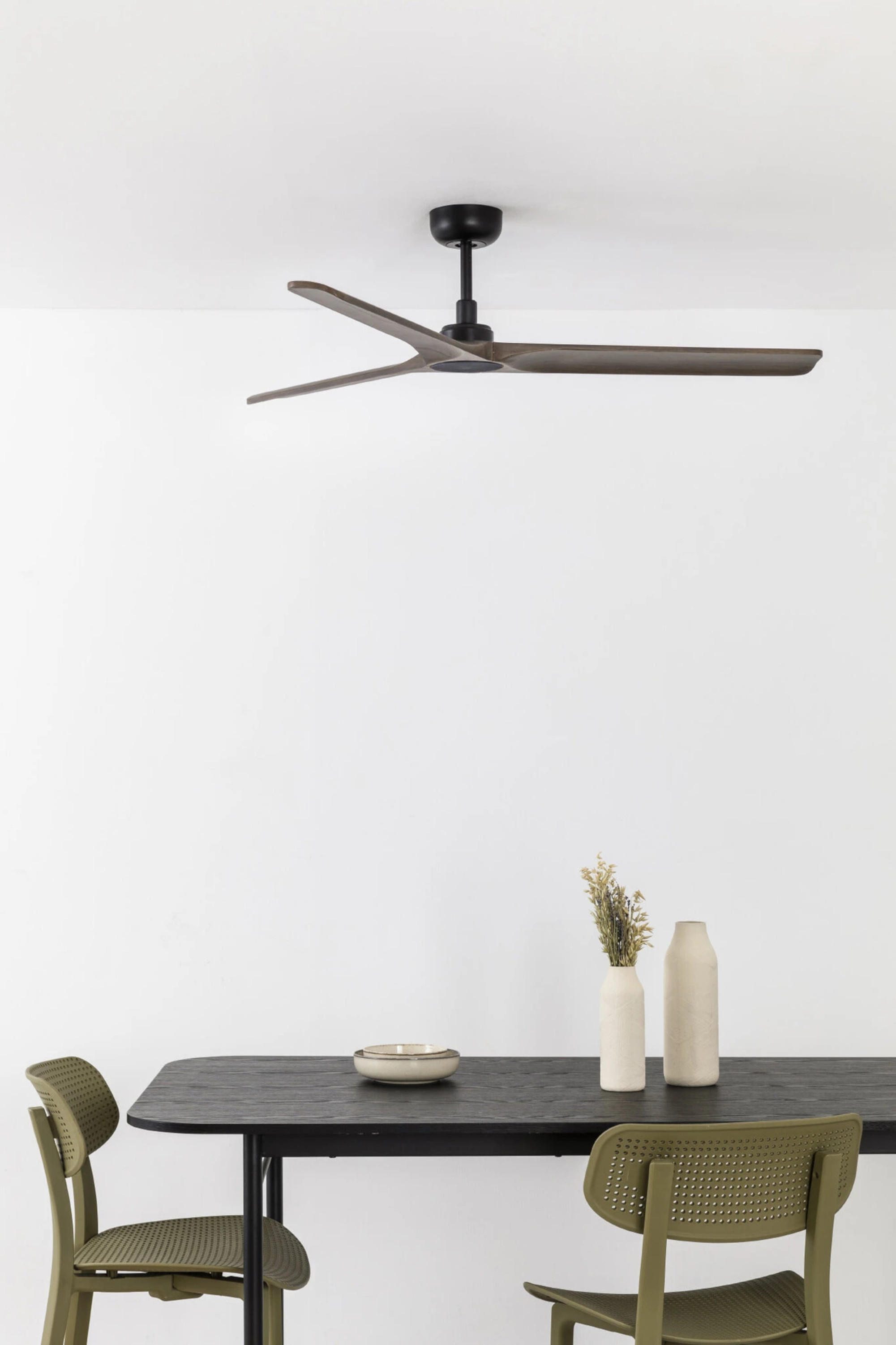 Esstisch mit zwei Stühlen, Deckenventilator und Dekoration. Tisch schwarz, Stühle grün, Wand weiß.
