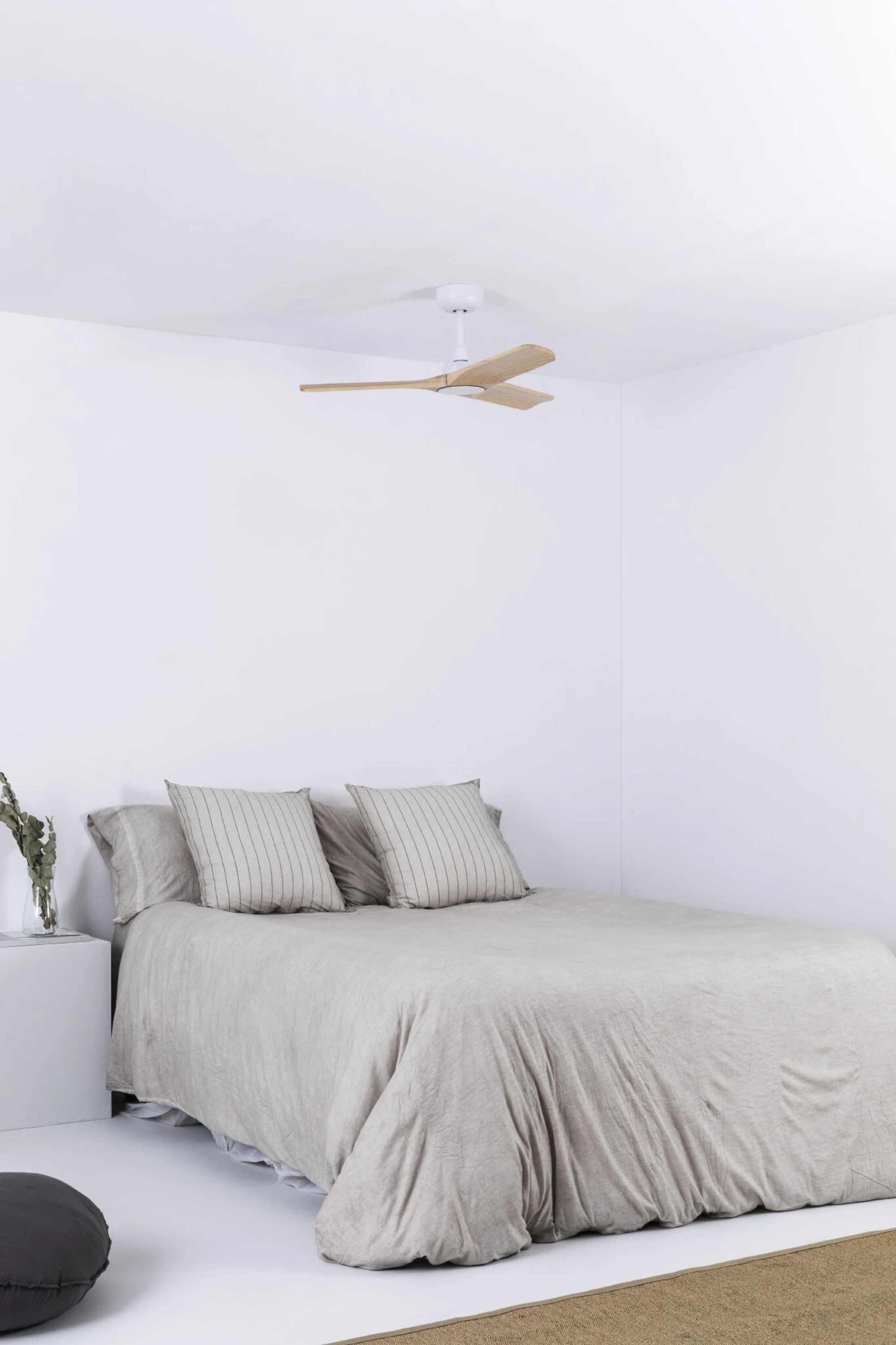 Schlafzimmer mit Bett, Kissen und Deckenventilator vor weißem Hintergrund.