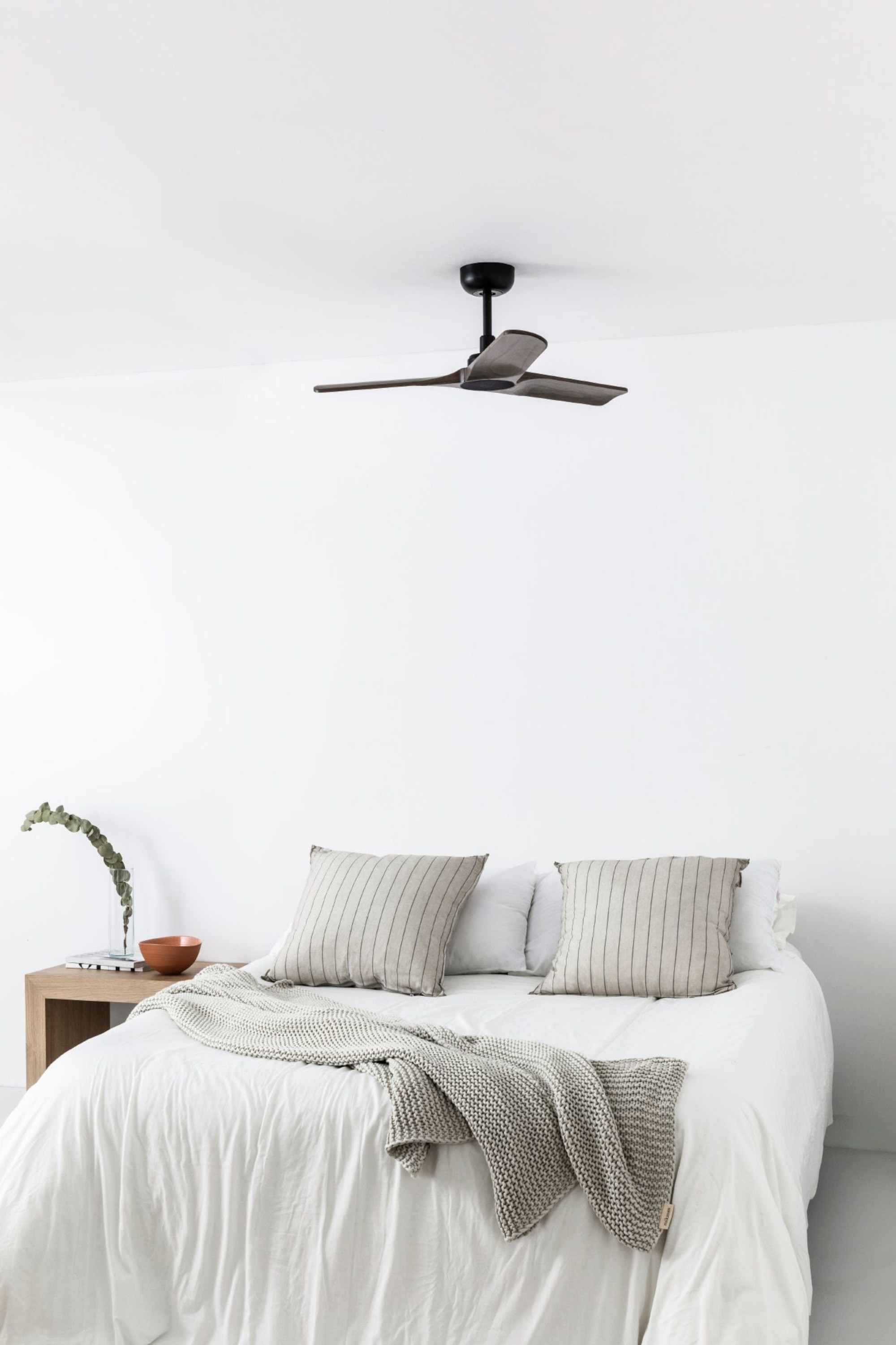 Schlafzimmer mit Deckenventilator, Bett, Kissen und Decke. Weiße Wände.