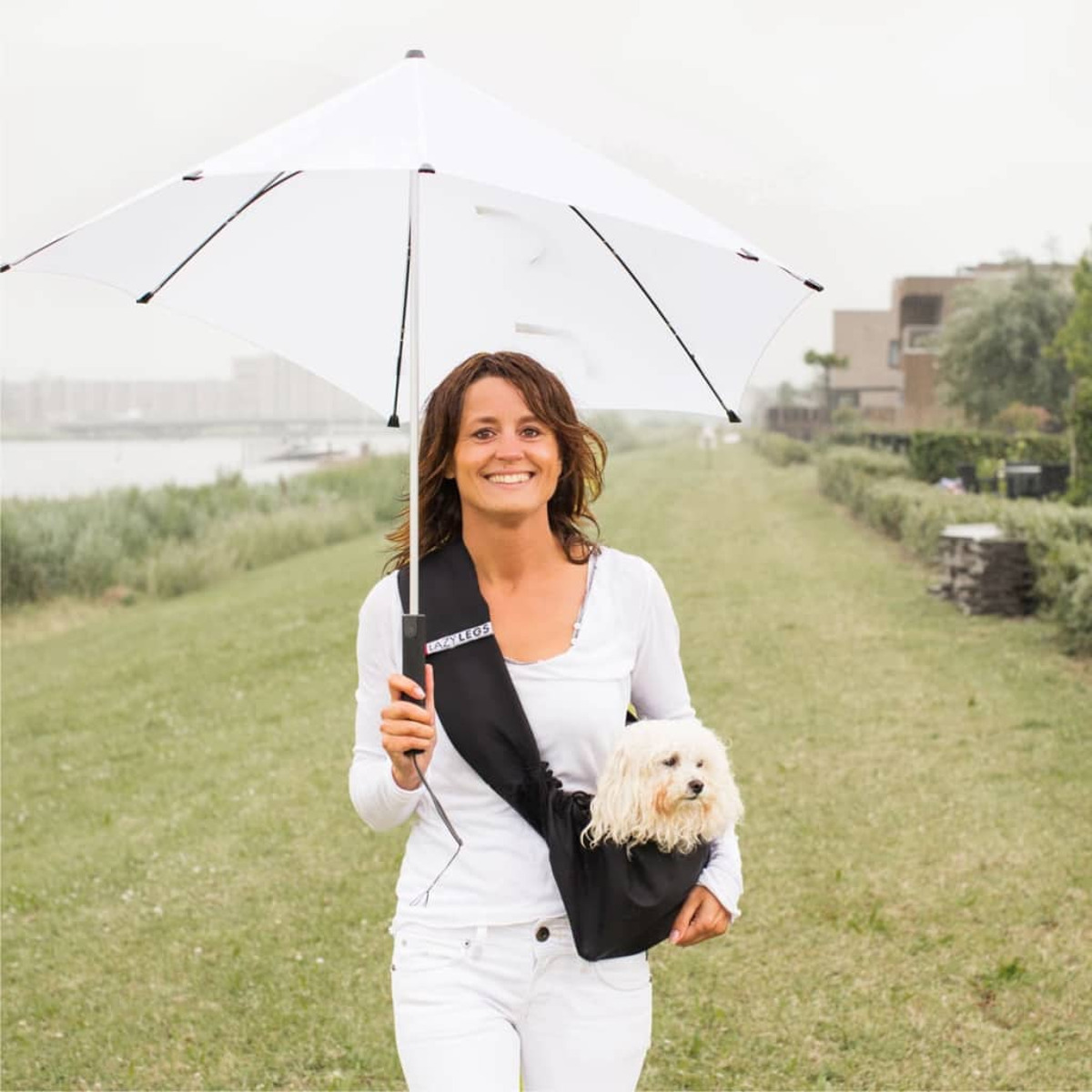 Eine Frau hält einen weißen Regenschirm und einen kleinen Hund in einer schwarzen Tasche.