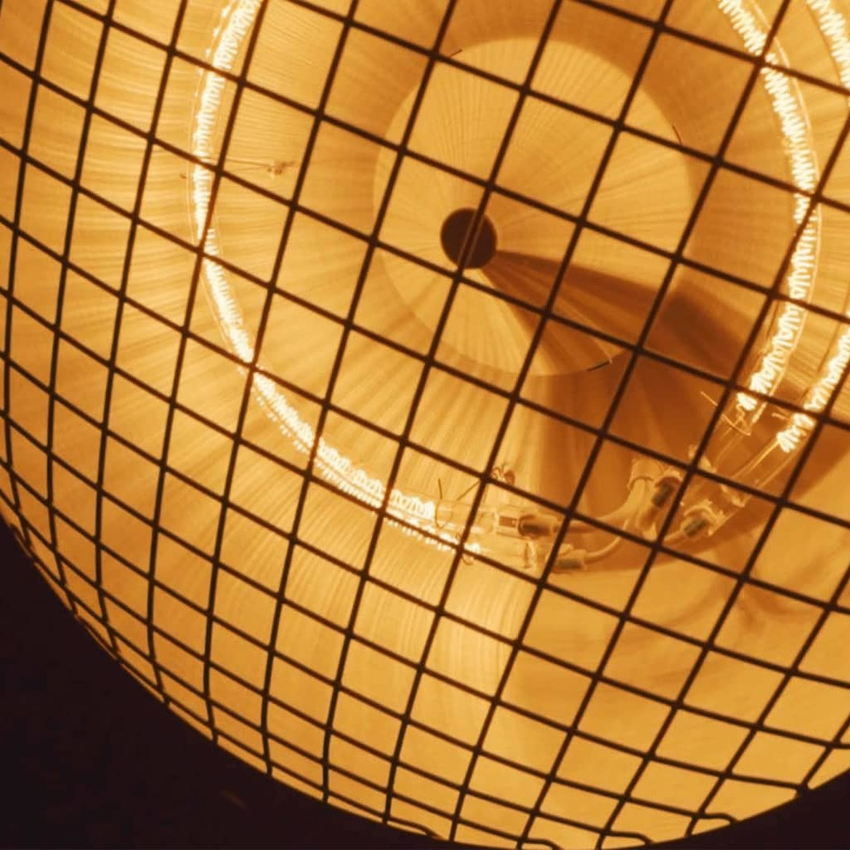 Close-up van een verwarmingselement beschermd door een metalen rooster, dat oranje licht uitstraalt.