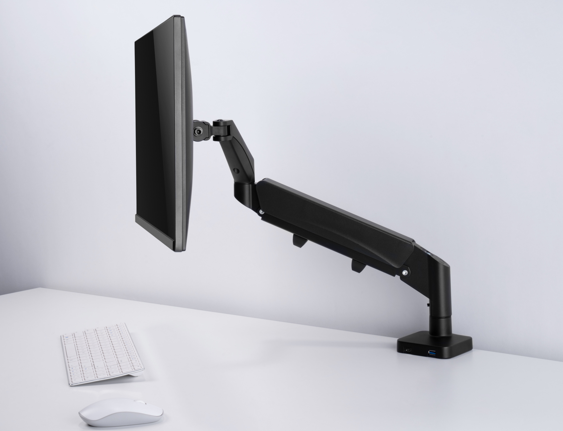 Schwarzer Computermonitor an einem schwarzen, verstellbaren Arm, weißer Schreibtisch, Tastatur und Maus.