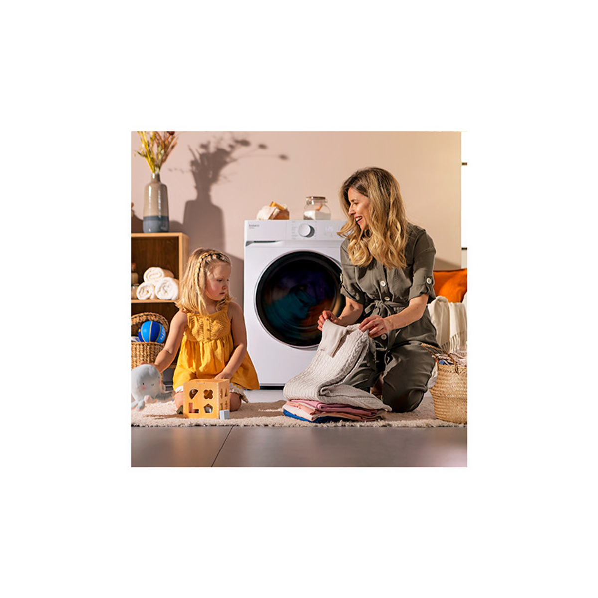 Kobieta i dziecko w pokoju z pralką i złożonymi ubraniami na dywanie.