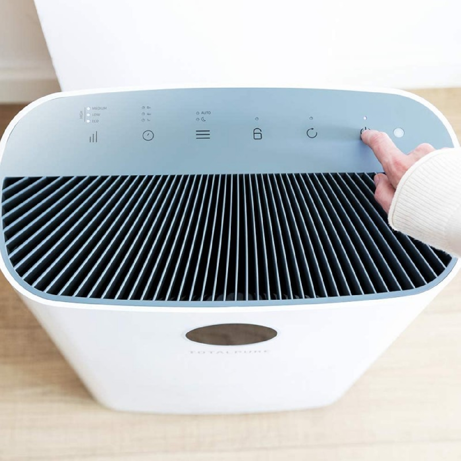 Una mano preme un pulsante su un purificatore d'aria bianco. Il purificatore ha una parte superiore con feritoie nere.
