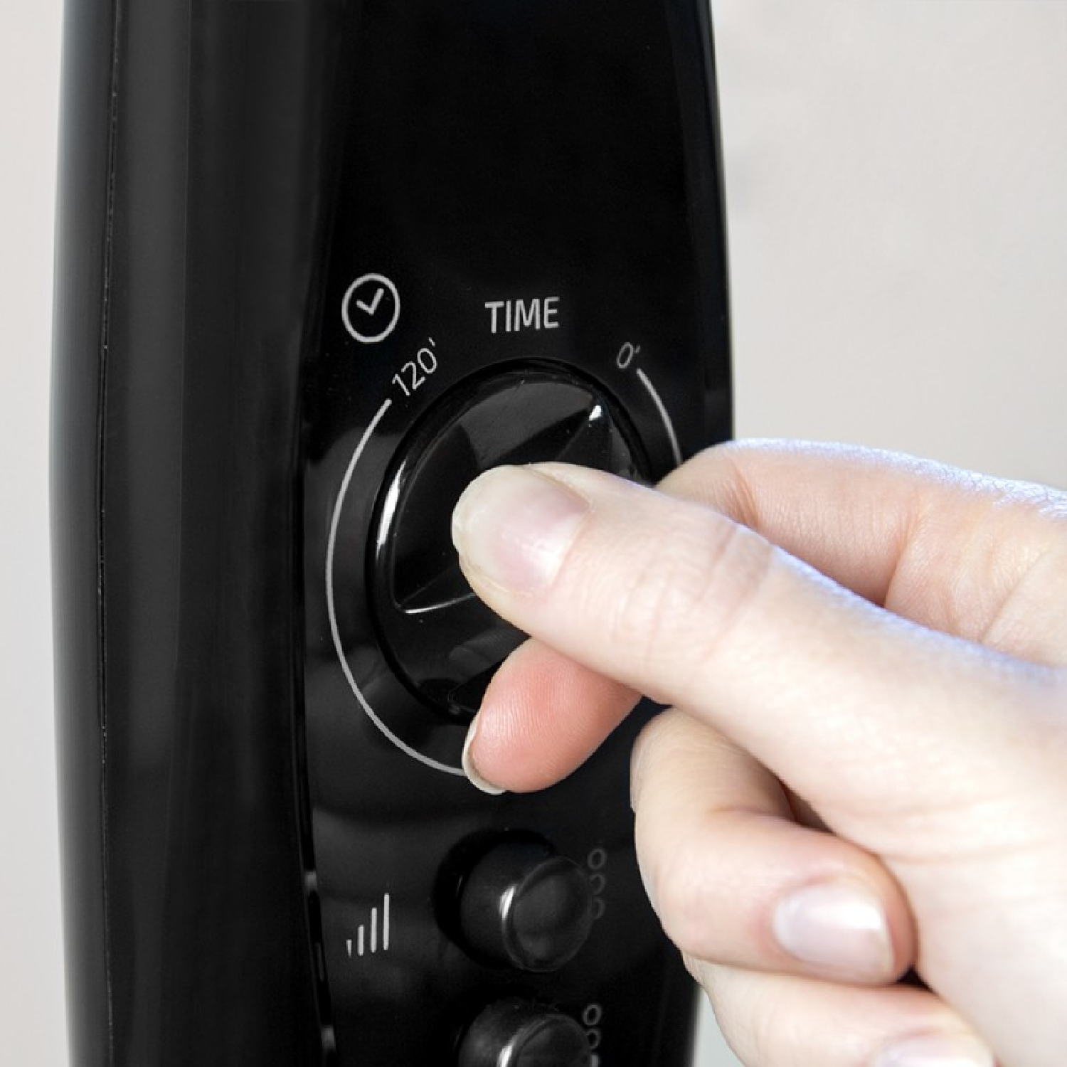 Dłoń regulująca pokrętło czarnego urządzenia. Widoczny wskaźnik czasu.