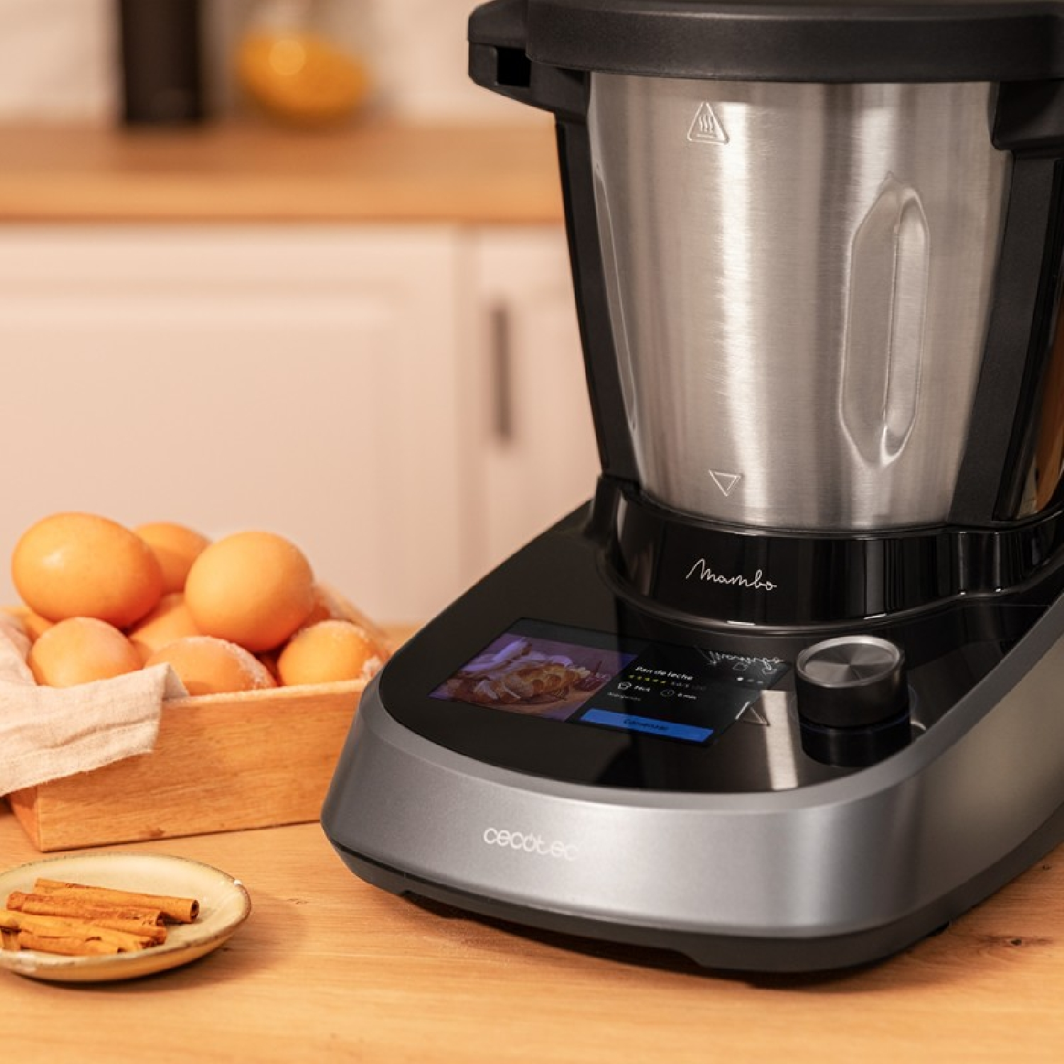 Un robot da cucina, con una ciotola in acciaio inossidabile. Ci sono uova, bastoncini di cannella e un tavolo di legno.