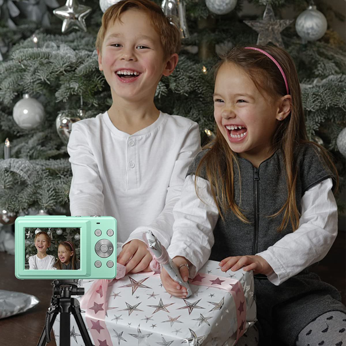 Dwoje dzieci śmieje się w pobliżu aparatu, prezentu i choinki.