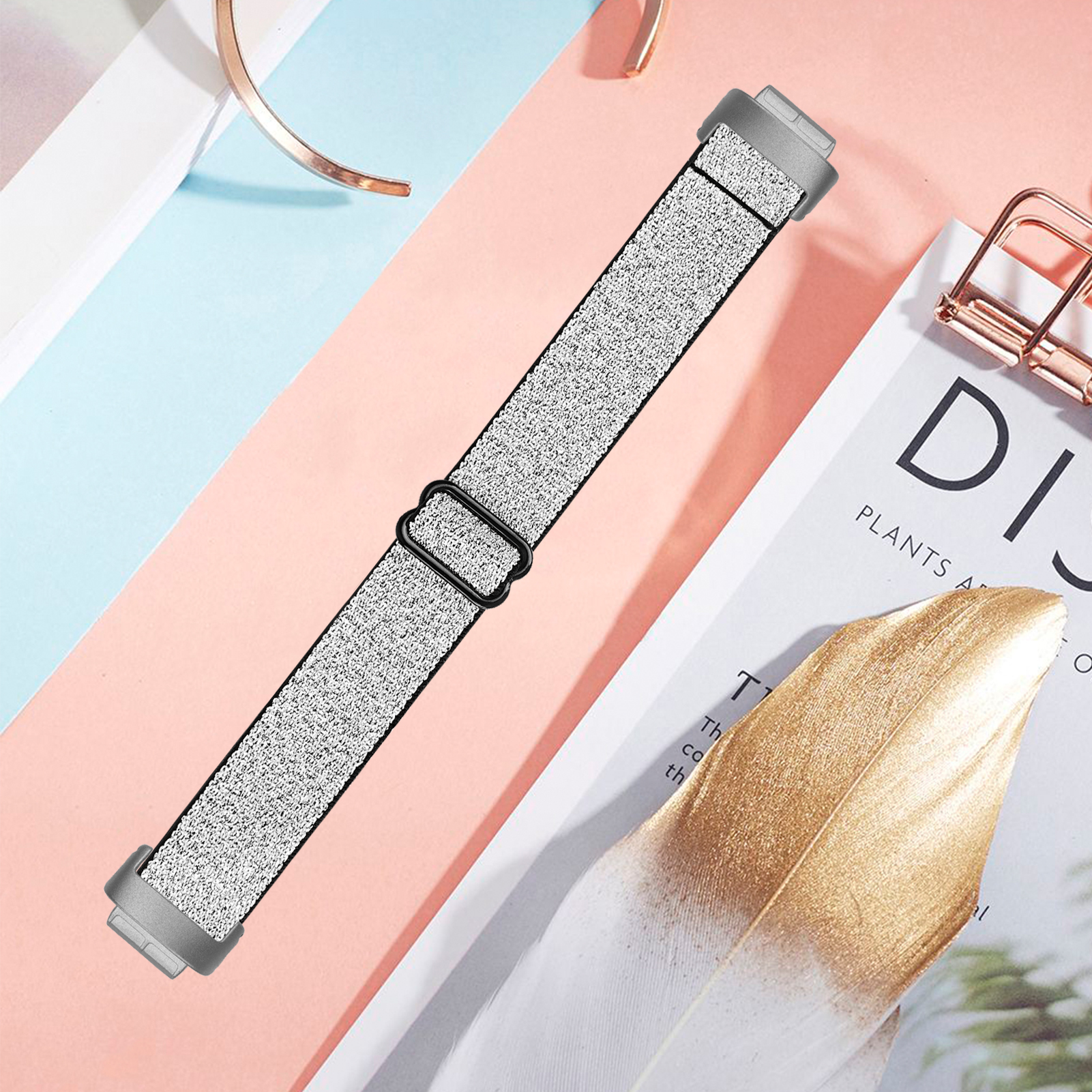 Ein graues Uhrenarmband ist auf einer Oberfläche mit goldenen Dekorationen und einer weißen Feder abgebildet.