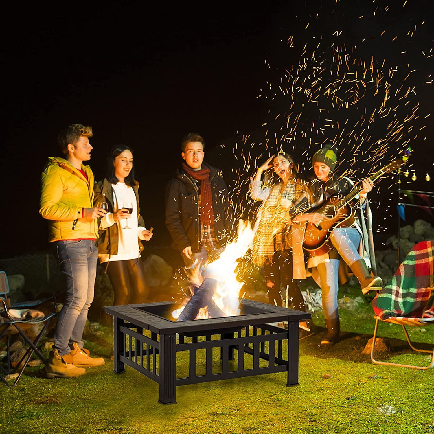 Gruppe von Leuten am Lagerfeuer bei Nacht. Flammen, Funken und eine Gitarre.