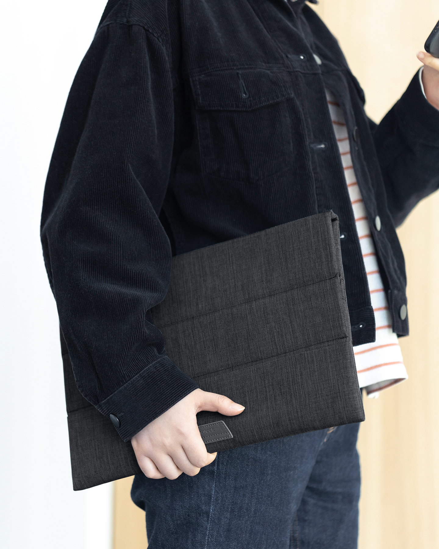 Eine Person hält eine dunkelgraue Tablethülle mit dunkler Jacke und Jeans.