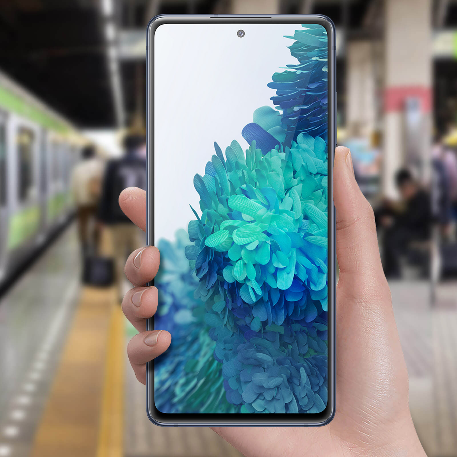 Una persona tiene in mano un telefono con display colorato e una stazione ferroviaria sullo sfondo.