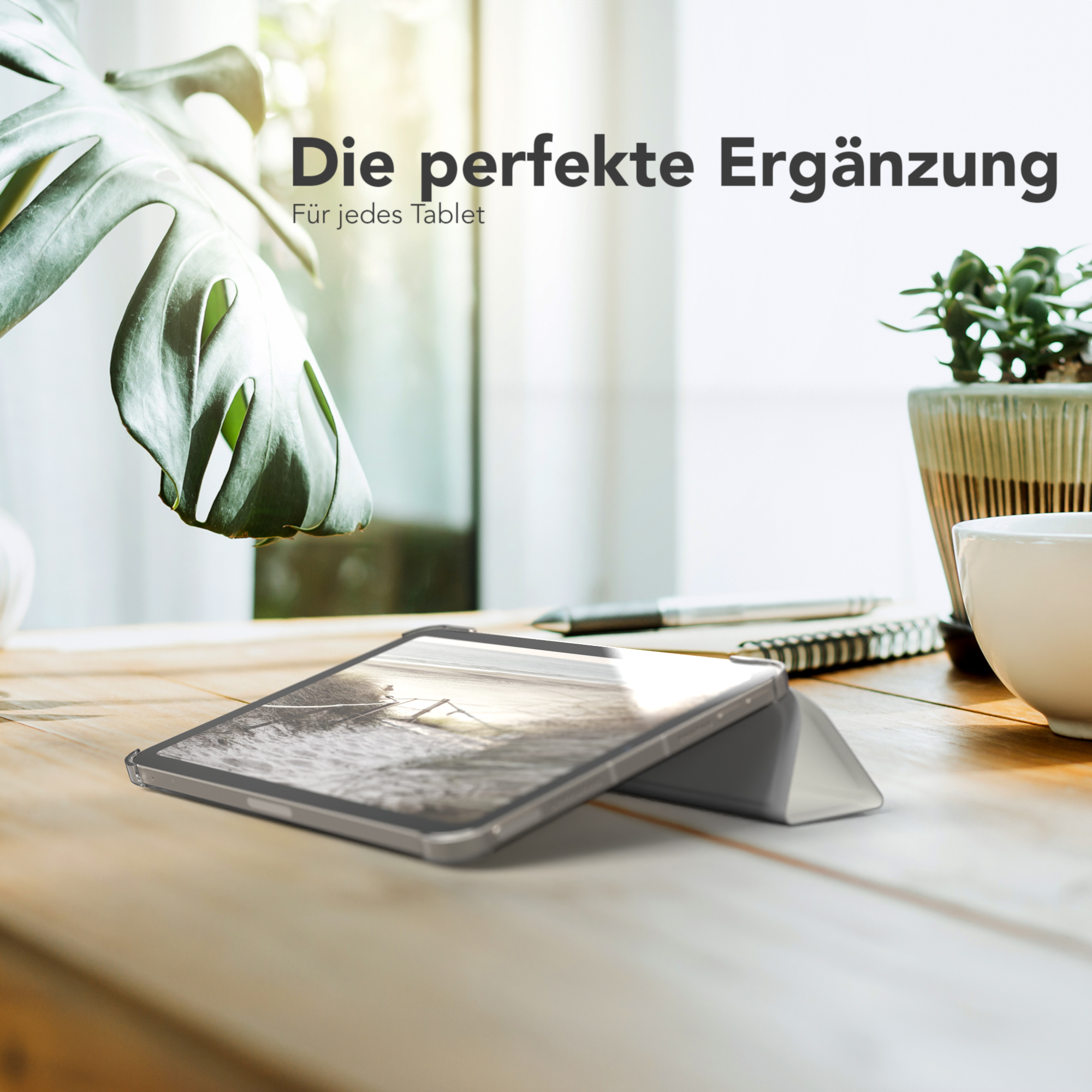 Ein Tablet mit Displayschutz in einer Hülle. Das Tablet steht auf einem Holztisch in der Nähe einer Pflanze.