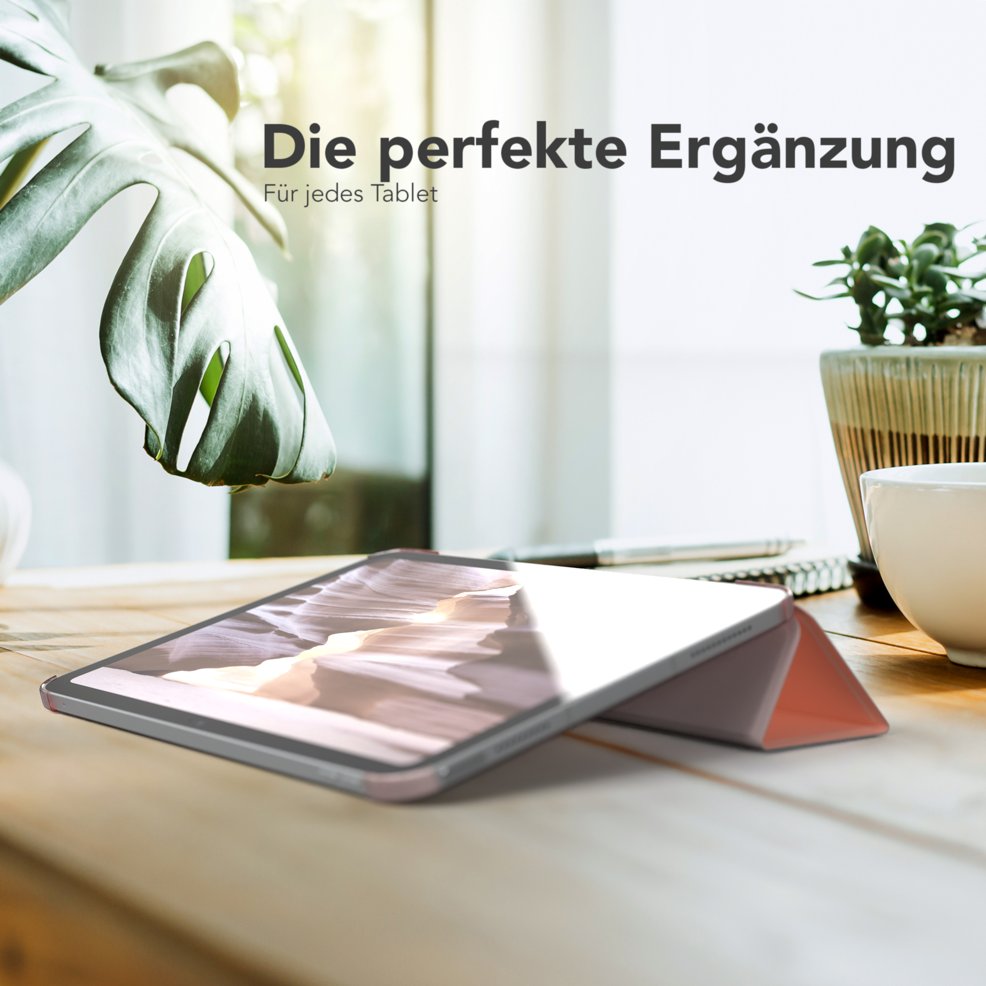 Tablet in einer Hülle mit Ständer auf einem Holztisch, eine Pflanze und eine Tasse stehen daneben.