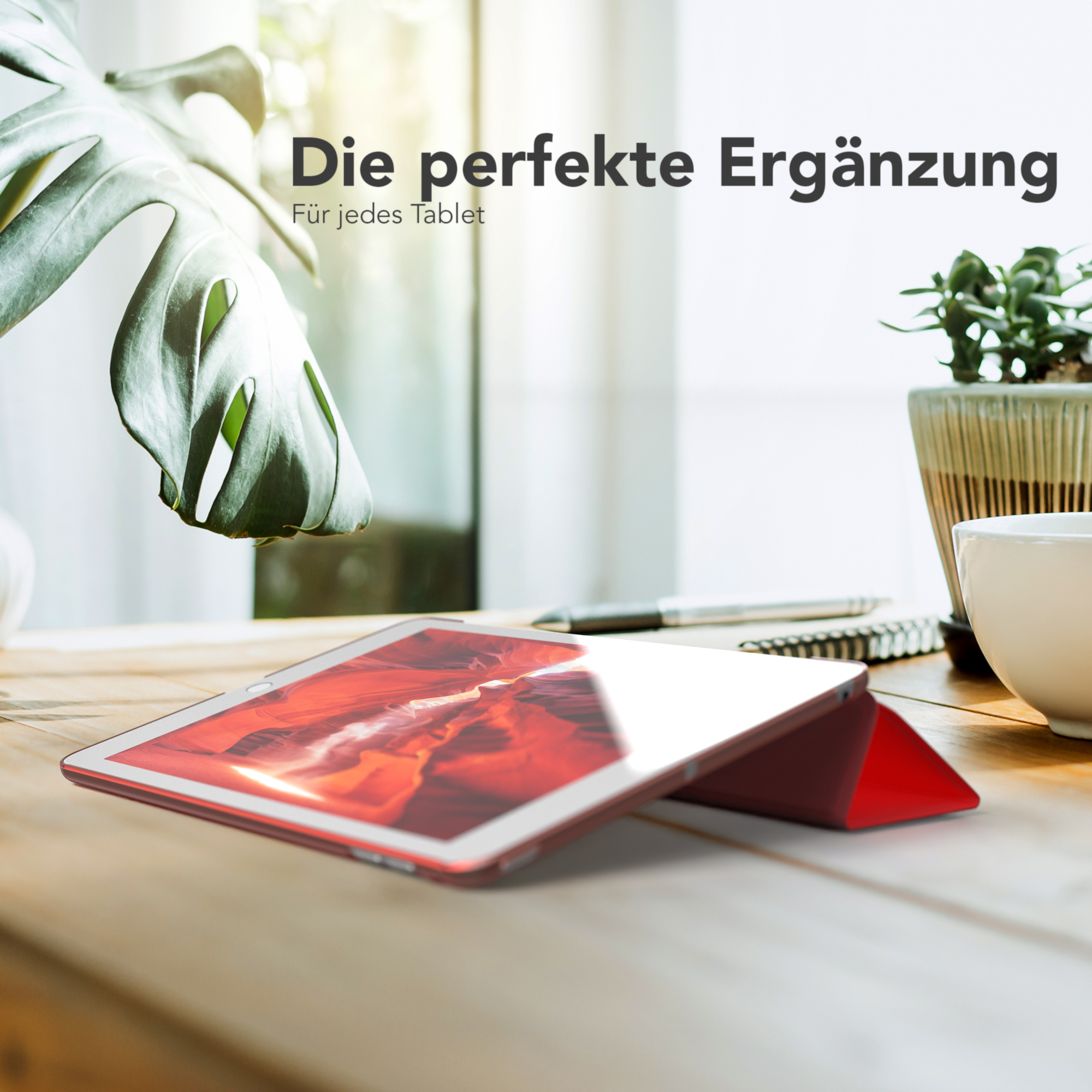 Tablet in roter Hülle auf Holztisch, neben Pflanze und Tasse.