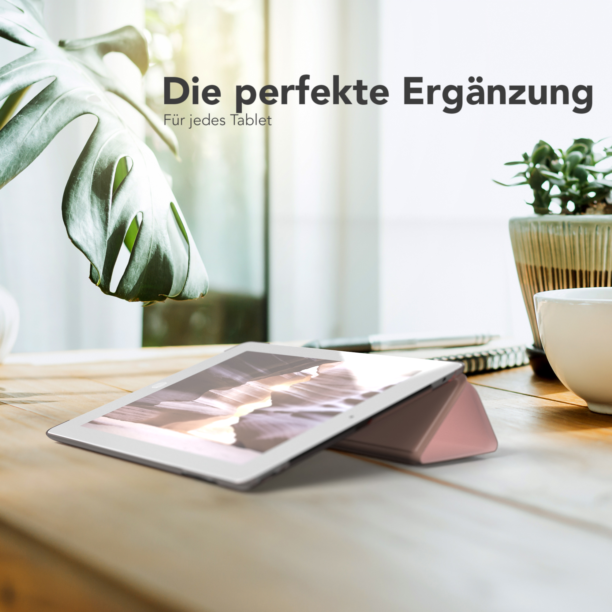Tablet mit rosa Hülle auf Holztisch, Pflanze im Topf, Fenster im Hintergrund.