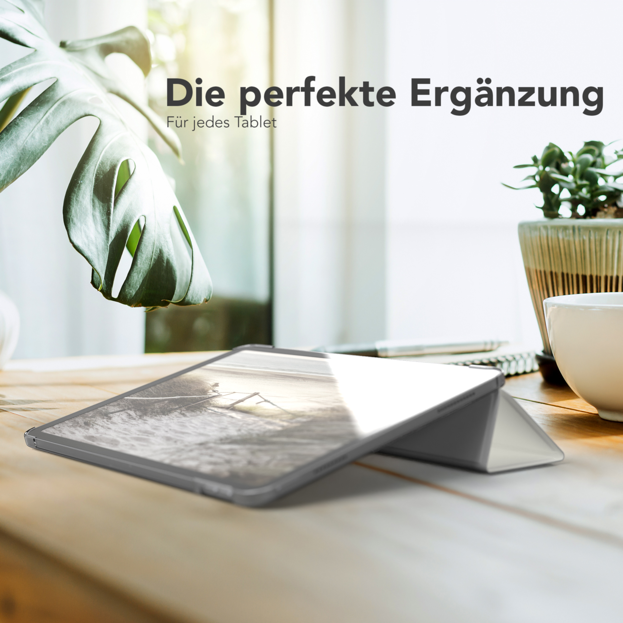 Tablet mit Displayschutz auf Holztisch. Im Hintergrund eine Pflanze.
