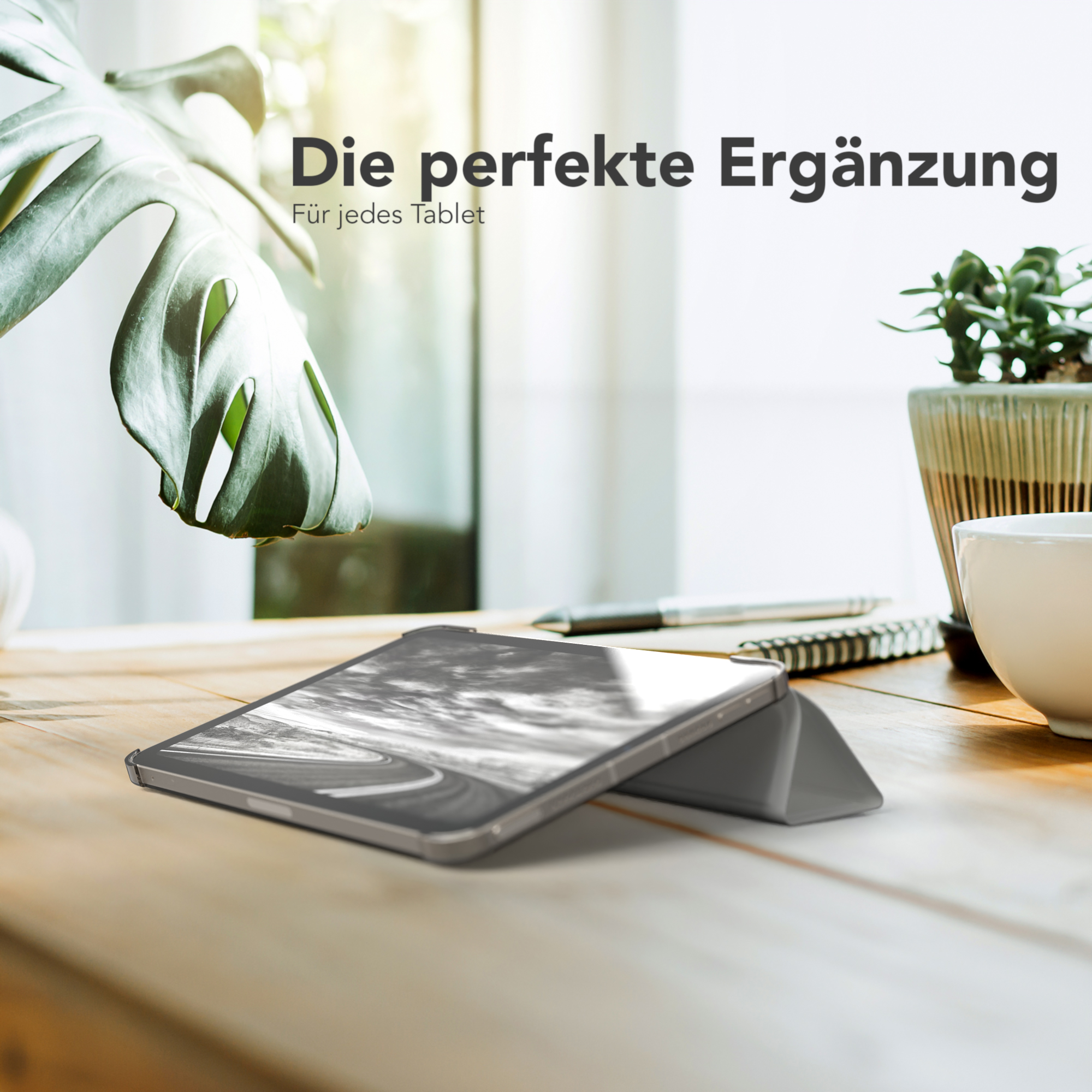 Tablet auf einem Holztisch mit grüner Hülle, mit einer Pflanze und einer Tasse.