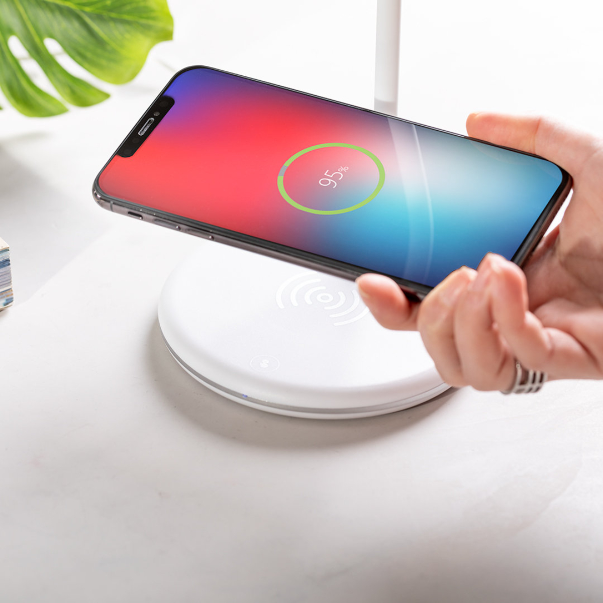 Una mano sostiene un teléfono sobre un cargador inalámbrico. El teléfono muestra un 95% de carga.